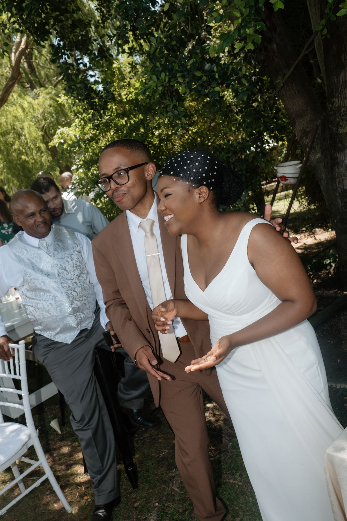 Smiling bride in white dress and groom in tan suit walking together at outdoor wedding ceremony.