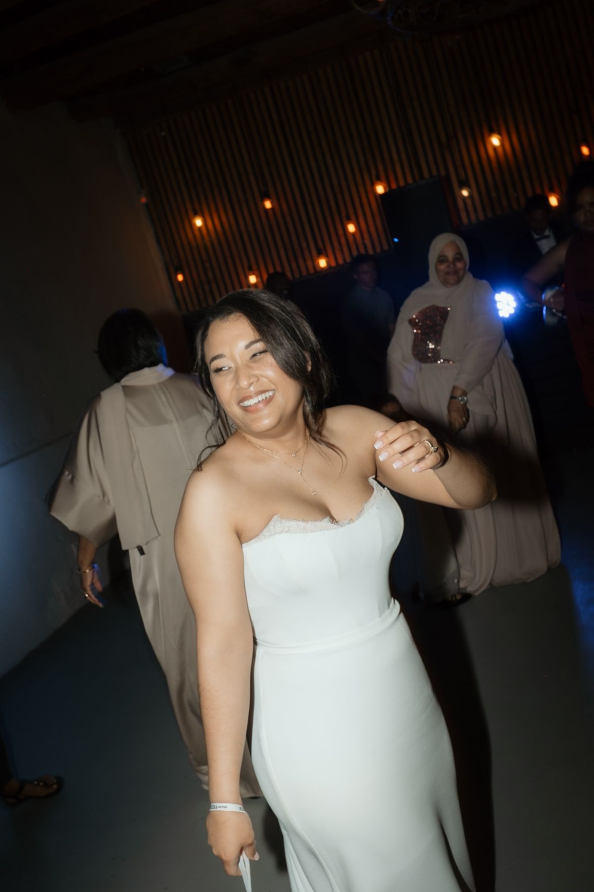 Woman in white dress smiling and dancing at wedding reception.