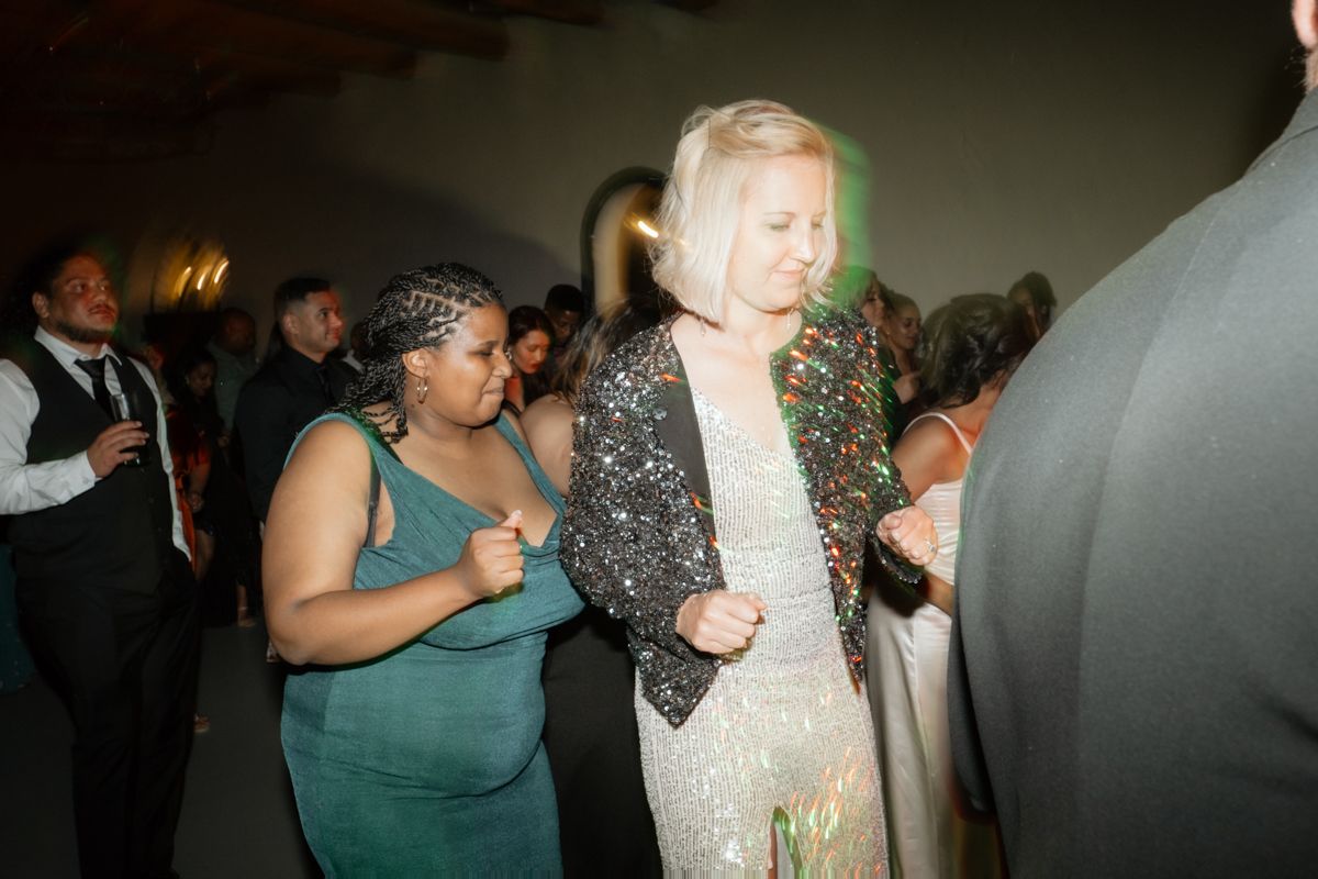 Two women dancing joyfully at a wedding reception in elegant evening attire.
