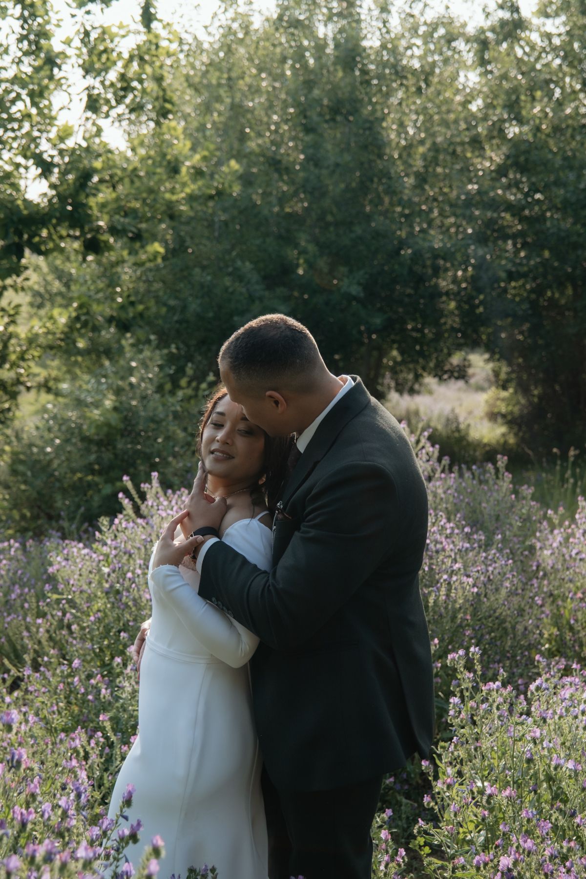 Bride and groom share a tender embrace in a field of purple lavender flowers at golden hour.