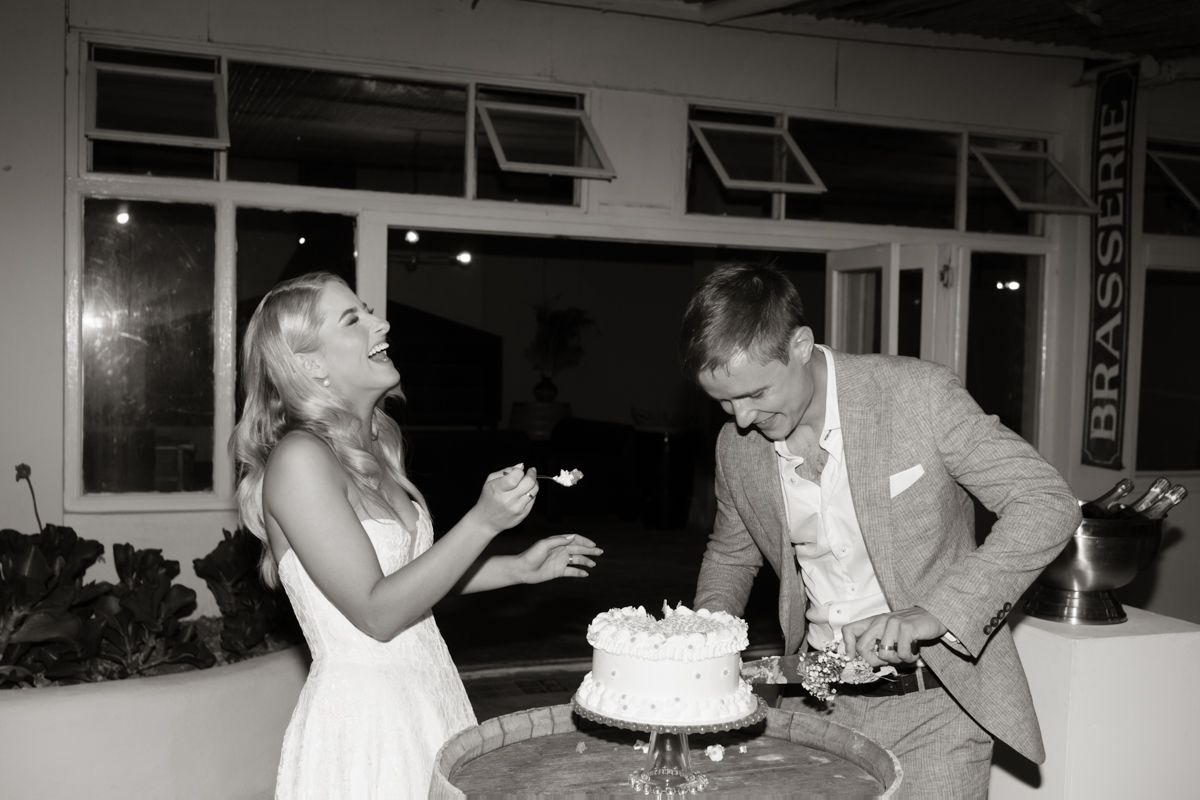 Bride and groom cutting white wedding cake together in black and white photo at evening reception.