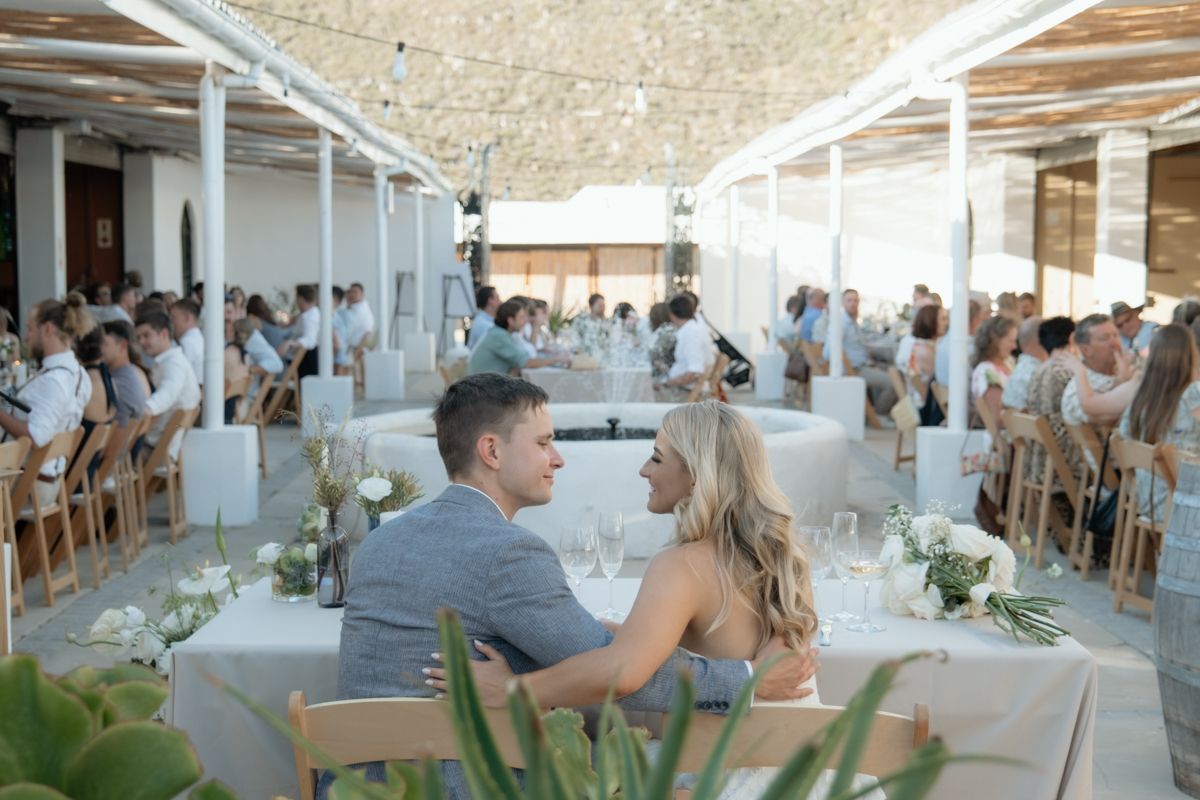 Bride and groom seated at sweetheart table during elegant outdoor wedding reception.