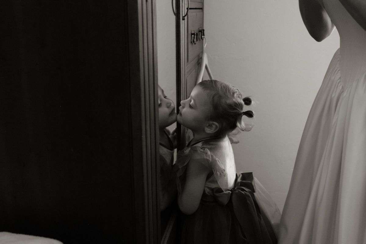 Black and white photo of a little girl in a tutu dress kissing her reflection in a mirror.