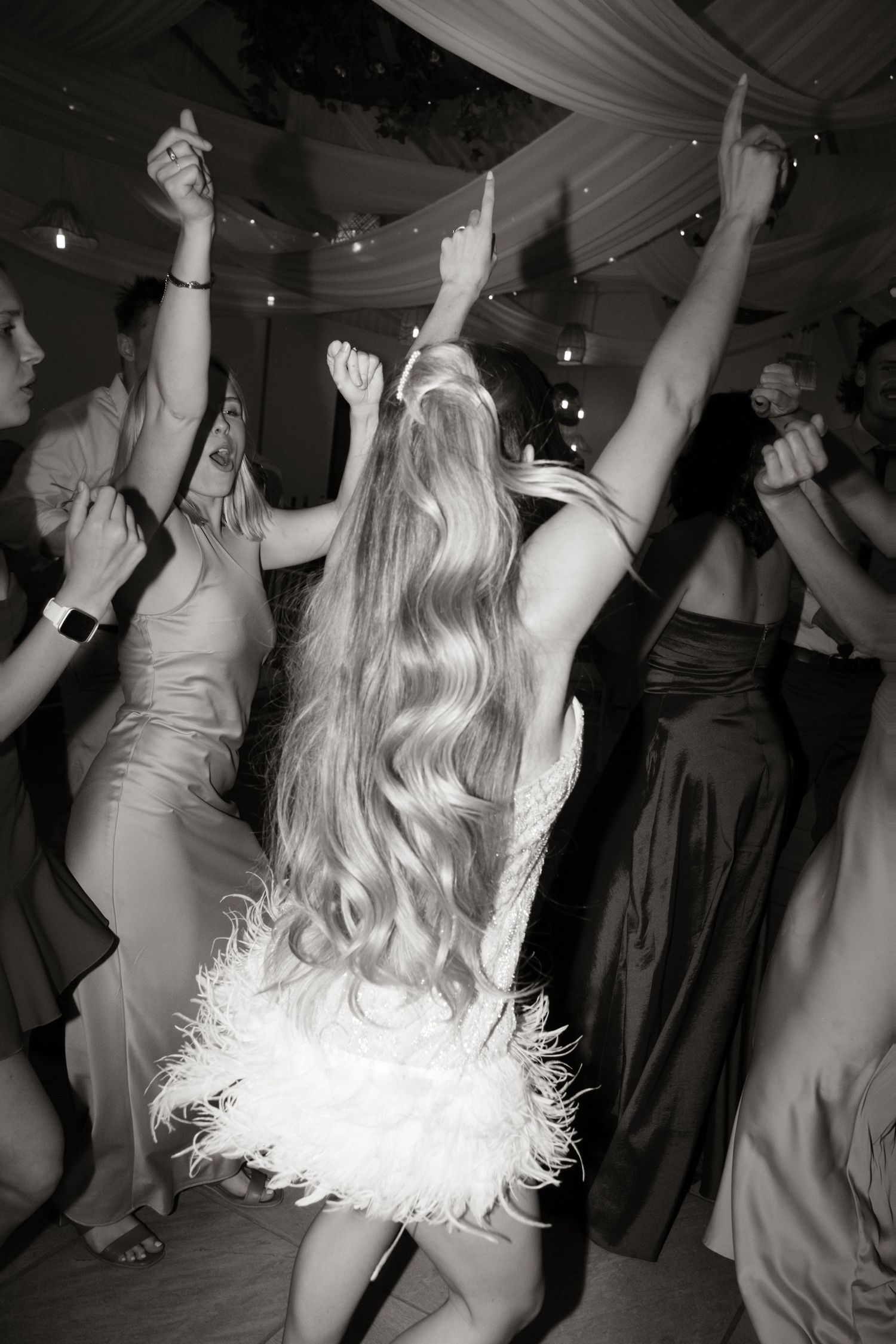 Black and white photo of bride with long blonde hair dancing joyfully at wedding reception party.