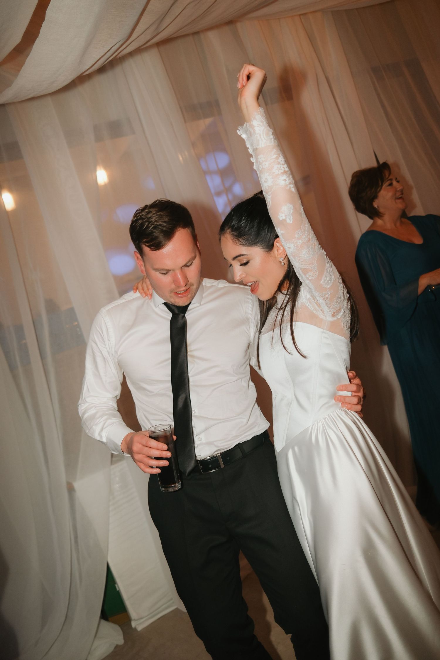 Bride and groom dance joyfully at their wedding reception, bride raising her arm.