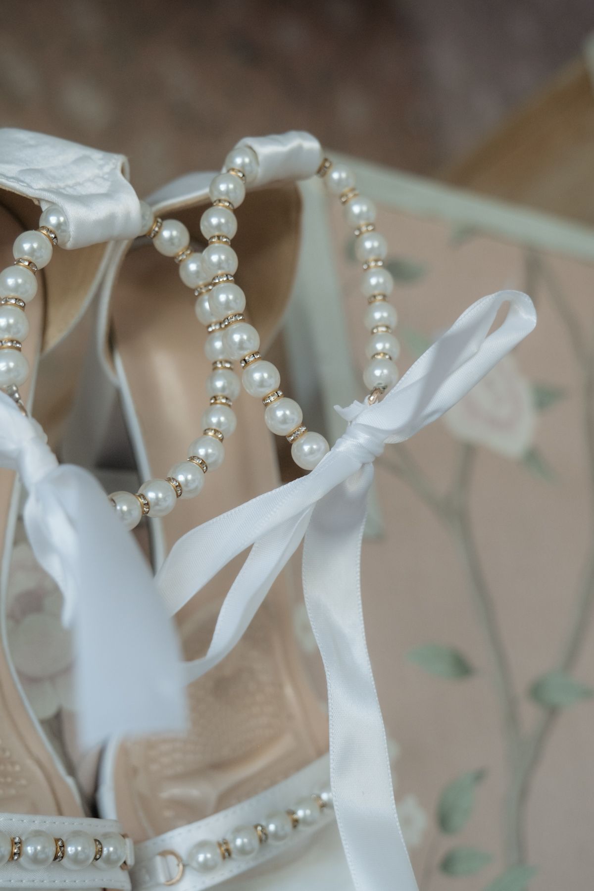 Elegant bridal shoes adorned with pearl straps and white satin ribbon bows in a decorative box.