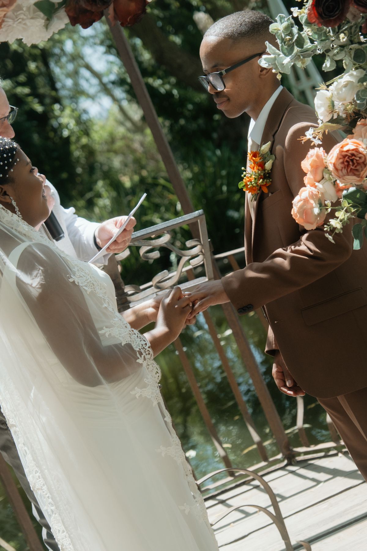 A bride and groom exchange rings at an outdoor wedding altar adorned with colorful floral arrangements.