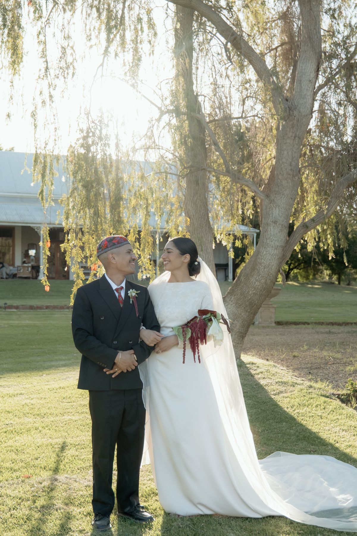 Bride and groom sharing a smile under a willow tree on their wedding day.