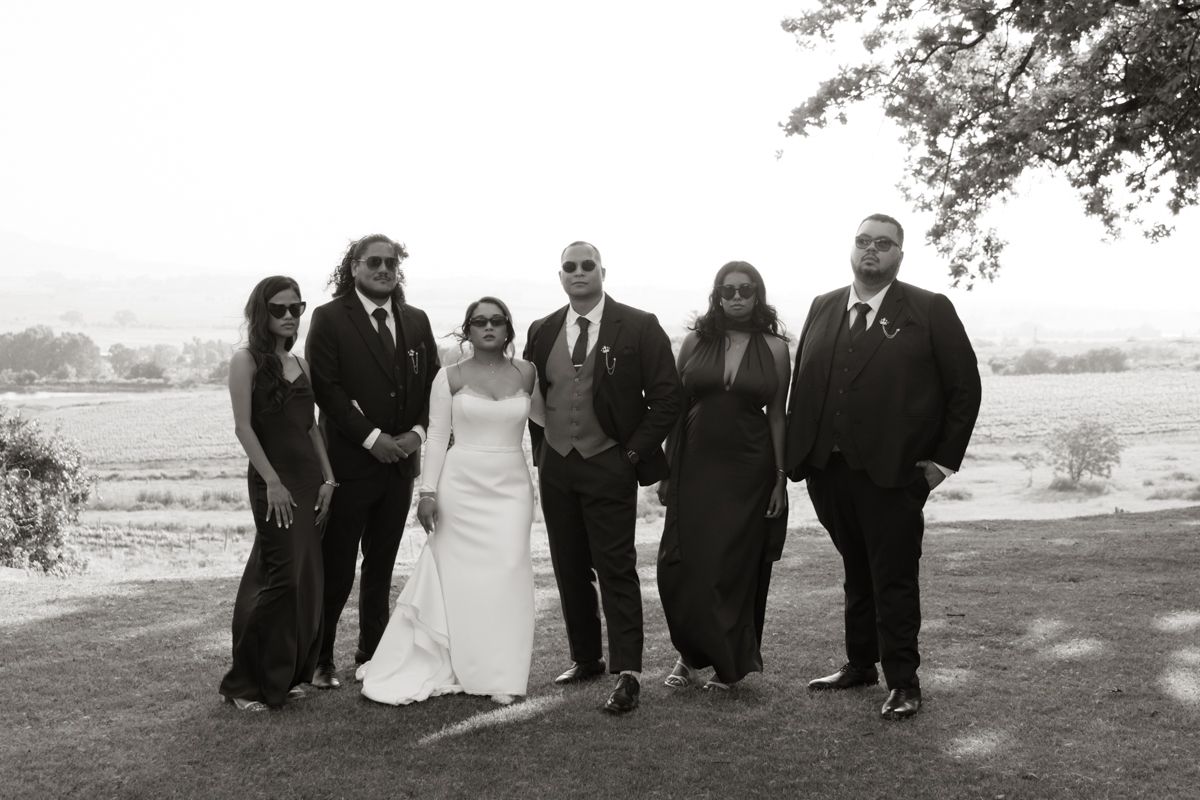 Wedding party group portrait in black and white on grassy hillside with scenic countryside landscape behind them.