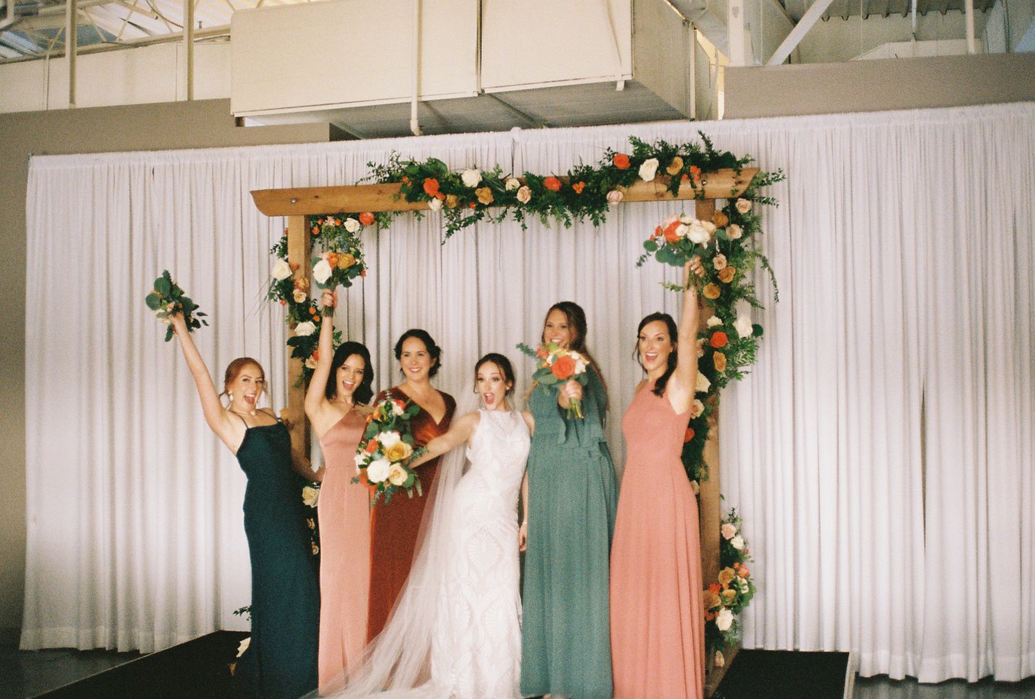 Bride and her 4 bridesmaids holding their bouquets up at the altar