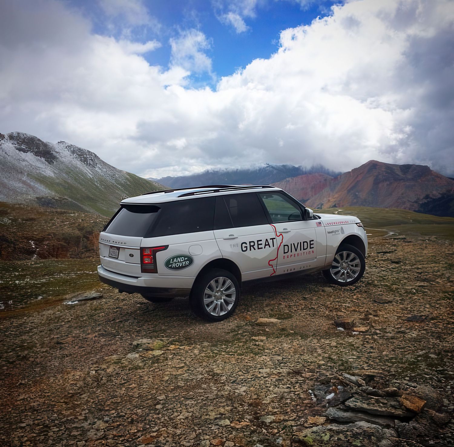 White Range Rover SUV with Great Divide branding parked on rocky mountain terrain under dramatic cloudy skies.