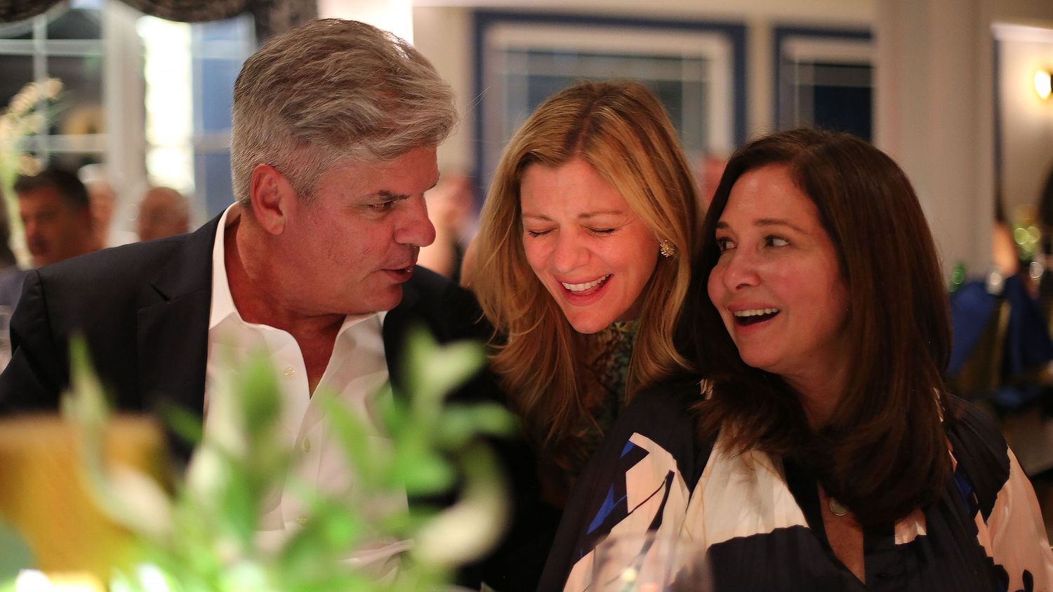 People gathered at a formal event sharing stories and smiles in warm lighting.