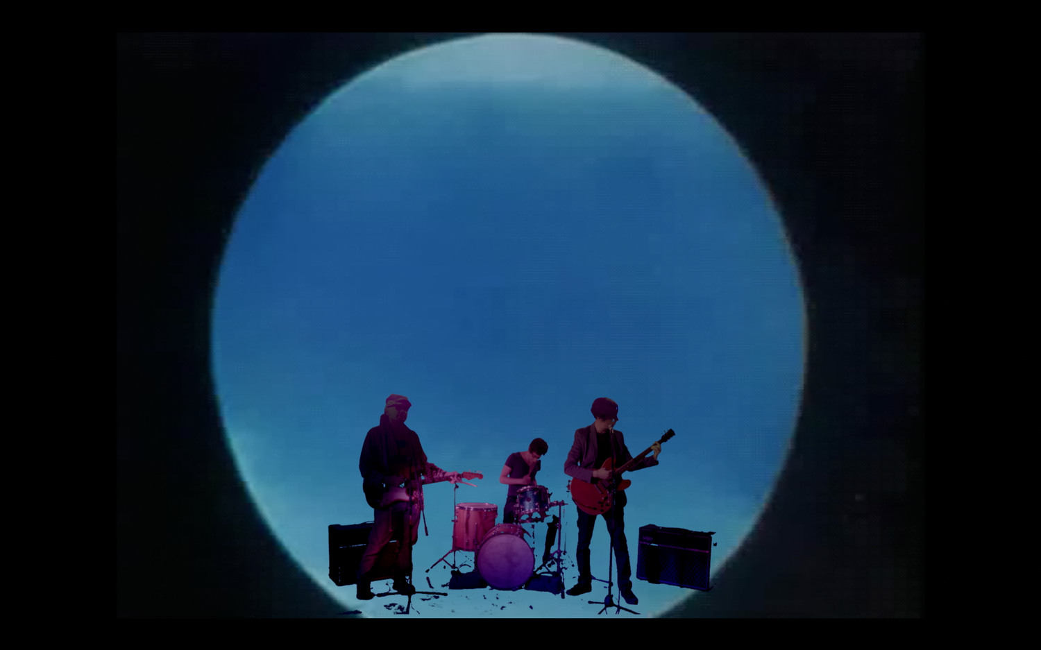 Band members silhouetted against a large circular blue backdrop during performance.