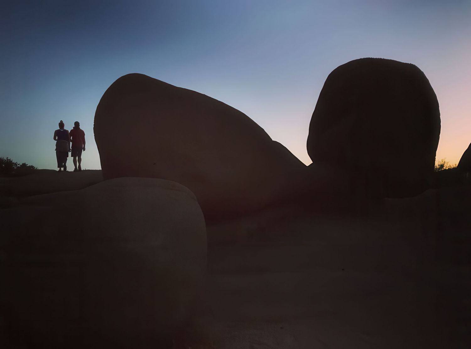Silhouettes of rock formations against a dusky sky during sunset.