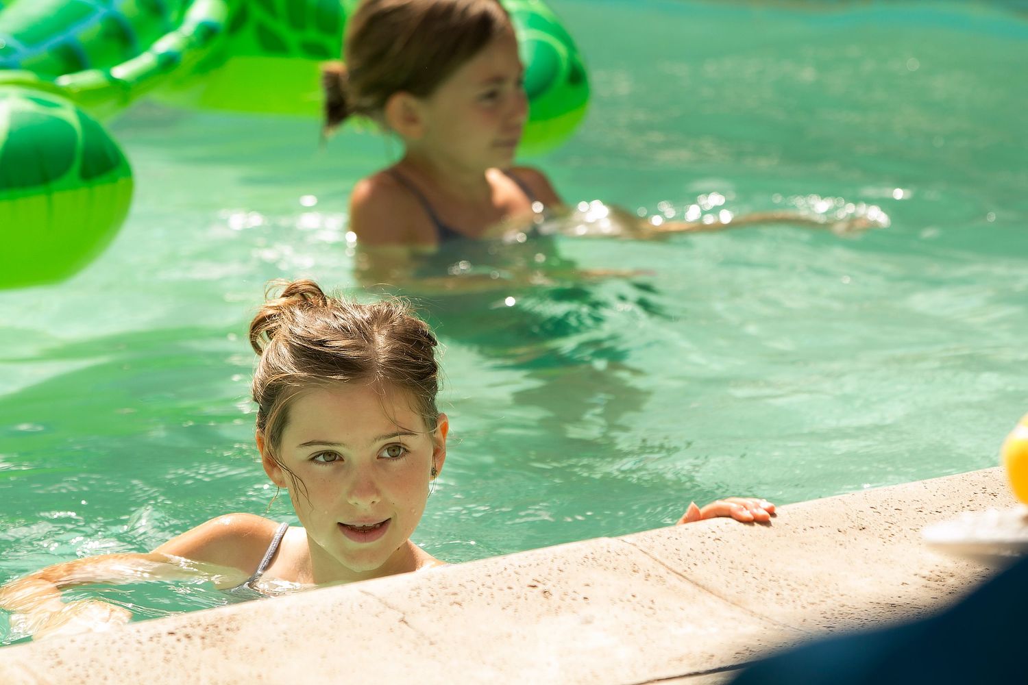 Children enjoying a refreshing swim in a bright turquoise pool on a sunny summer day.