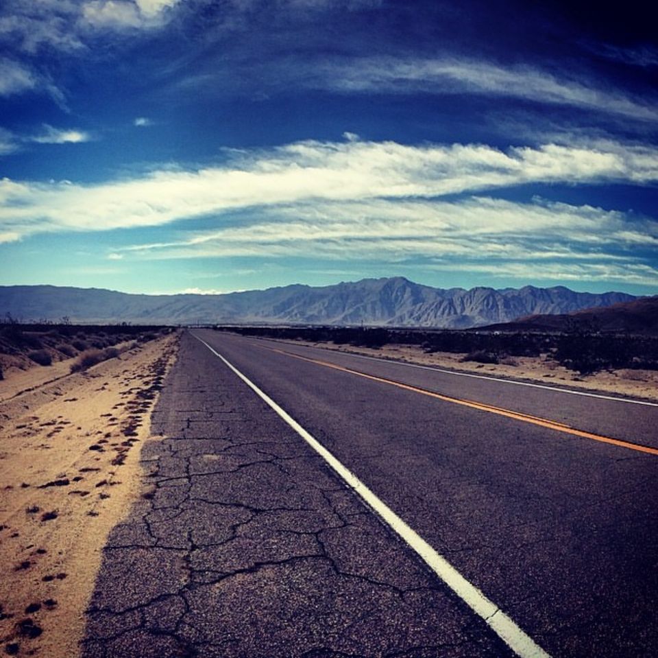 Desert highway stretching into distance with mountains and blue sky panorama.