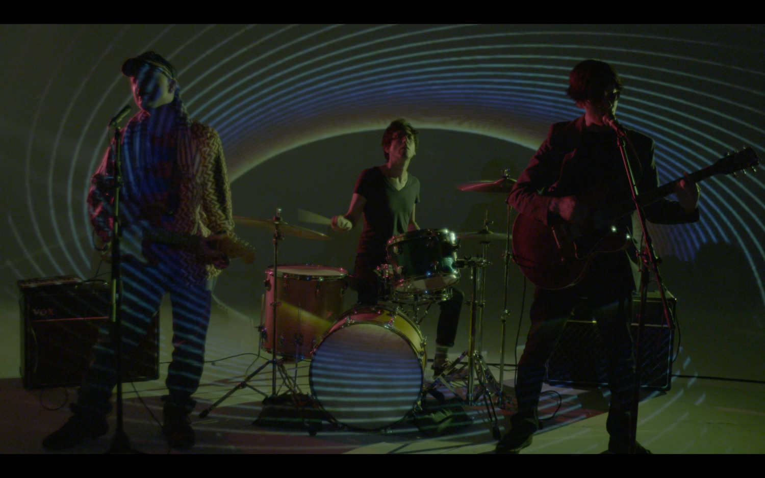 Band performing on stage with curved architectural elements and dramatic lighting.