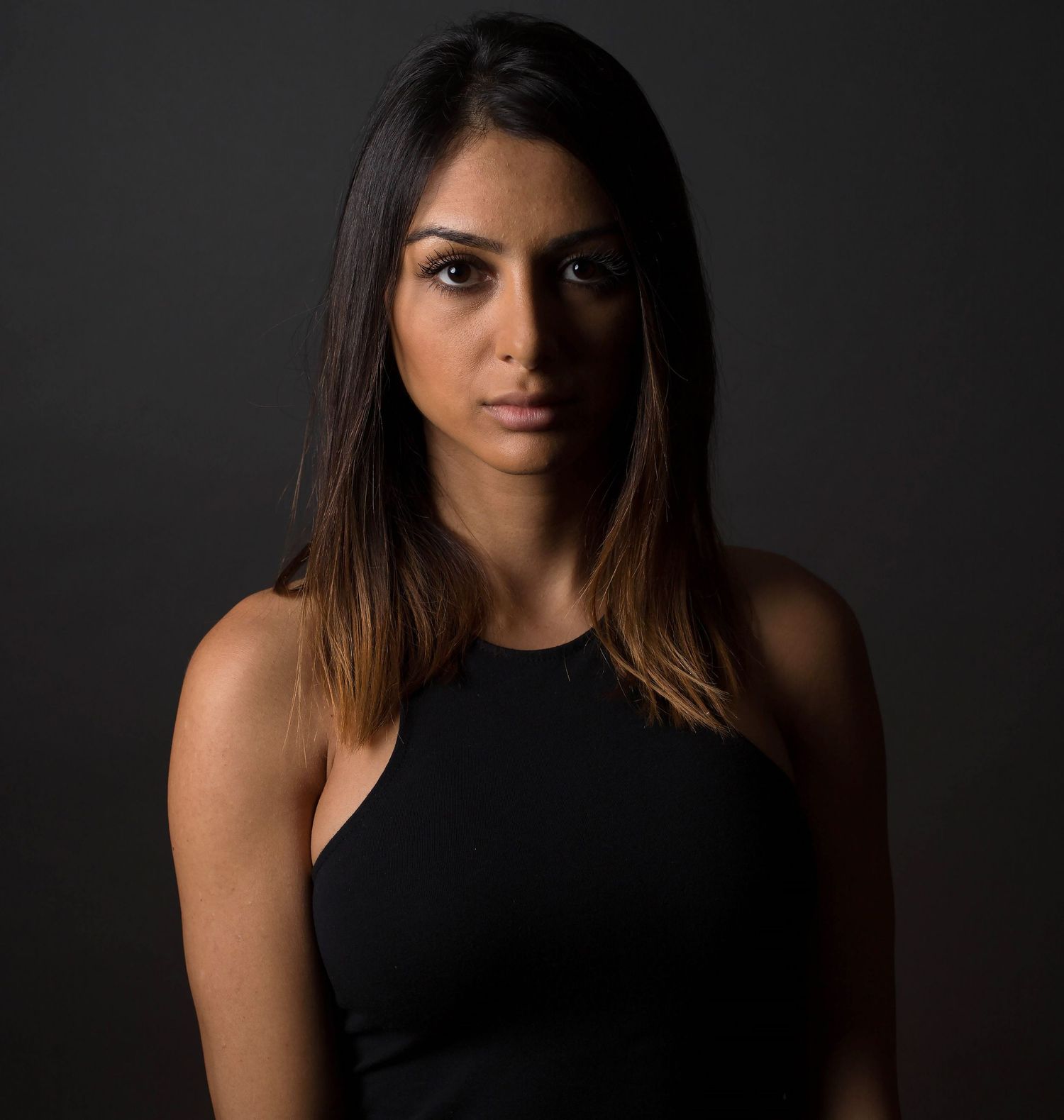 Woman in black top poses against dark background in moody portrait series.