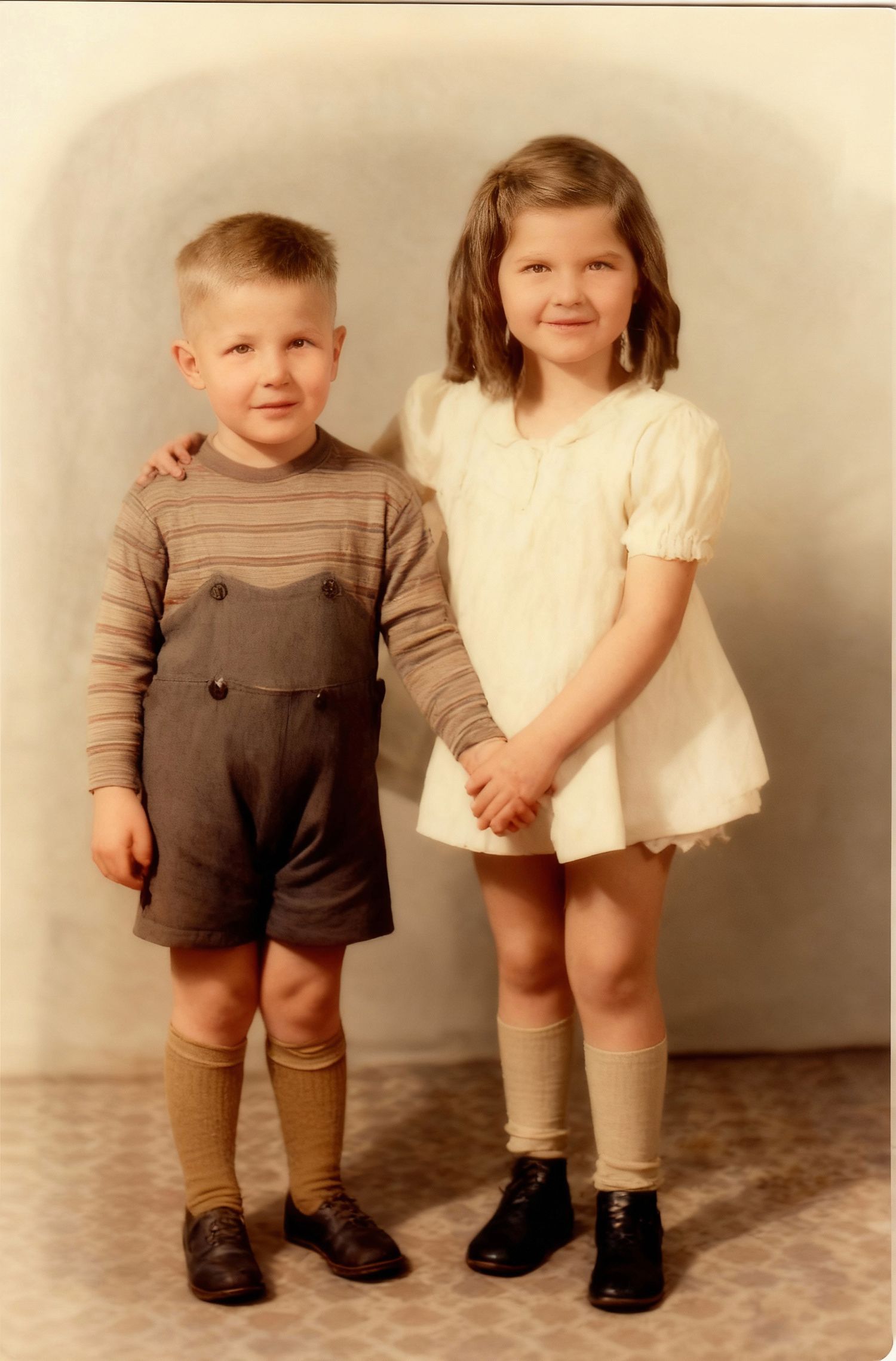 A vintage photograph of two children in formal attire from the 1950s, wearing knee socks and dress shoes.