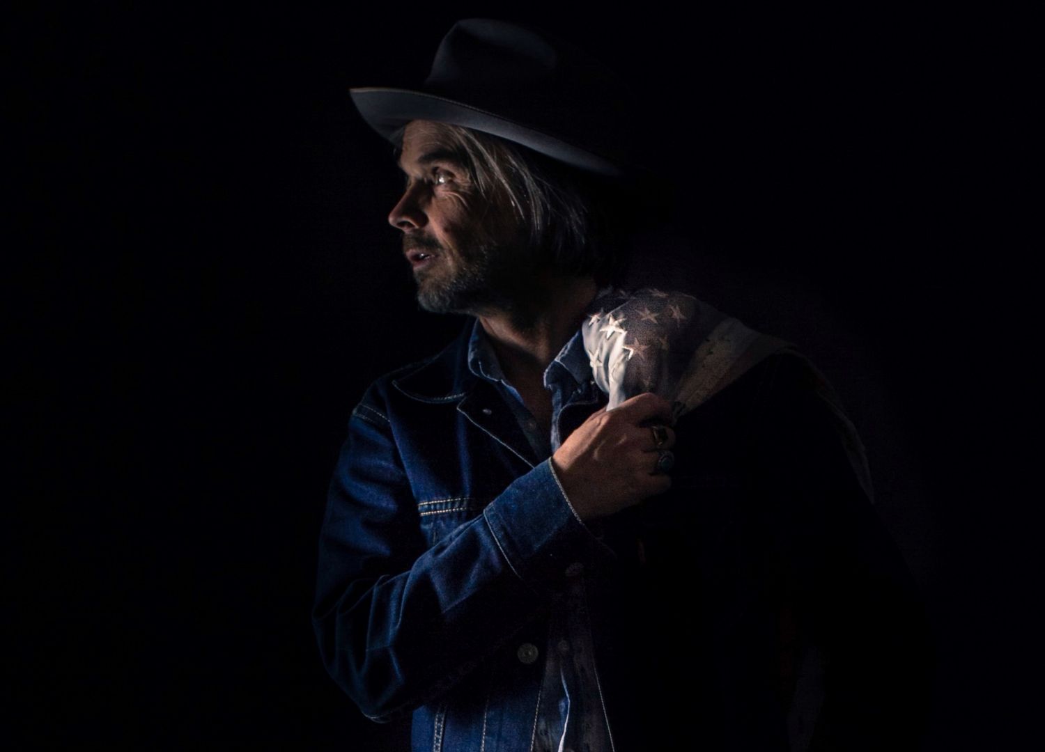 Person in denim jacket photographed in dramatic low-key lighting conditions.
