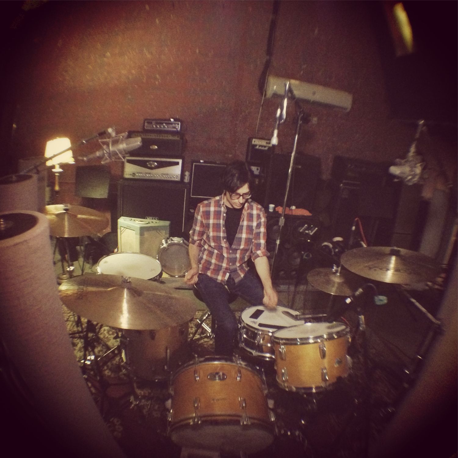 Drummer performing behind drum kit in dark concert venue with vintage film effect.