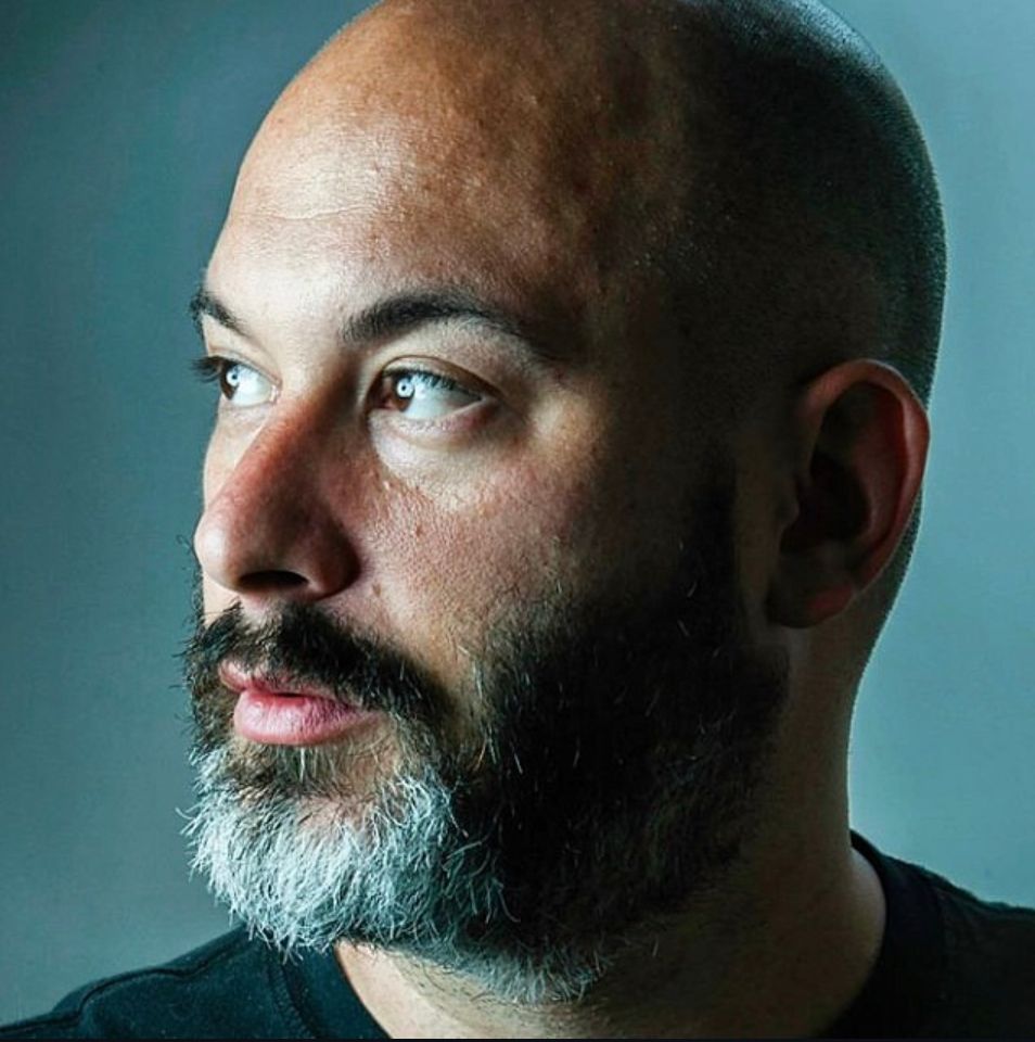 Profile view showing a bearded person in dramatic side lighting against a blue backdrop.