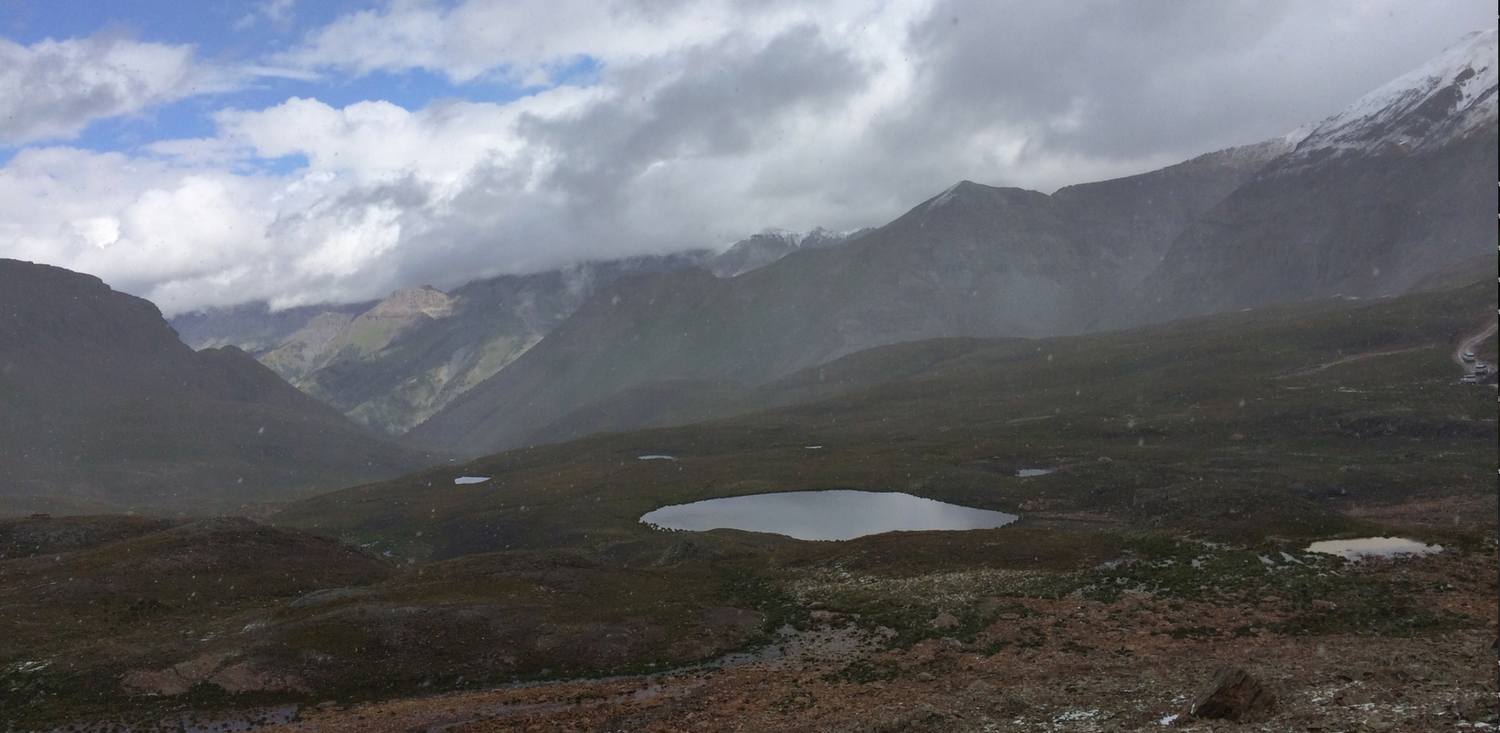 Panoramic view of misty mountain valley with alpine lakes, rugged terrain, and dramatic cloudy skies in a remote wilderness.