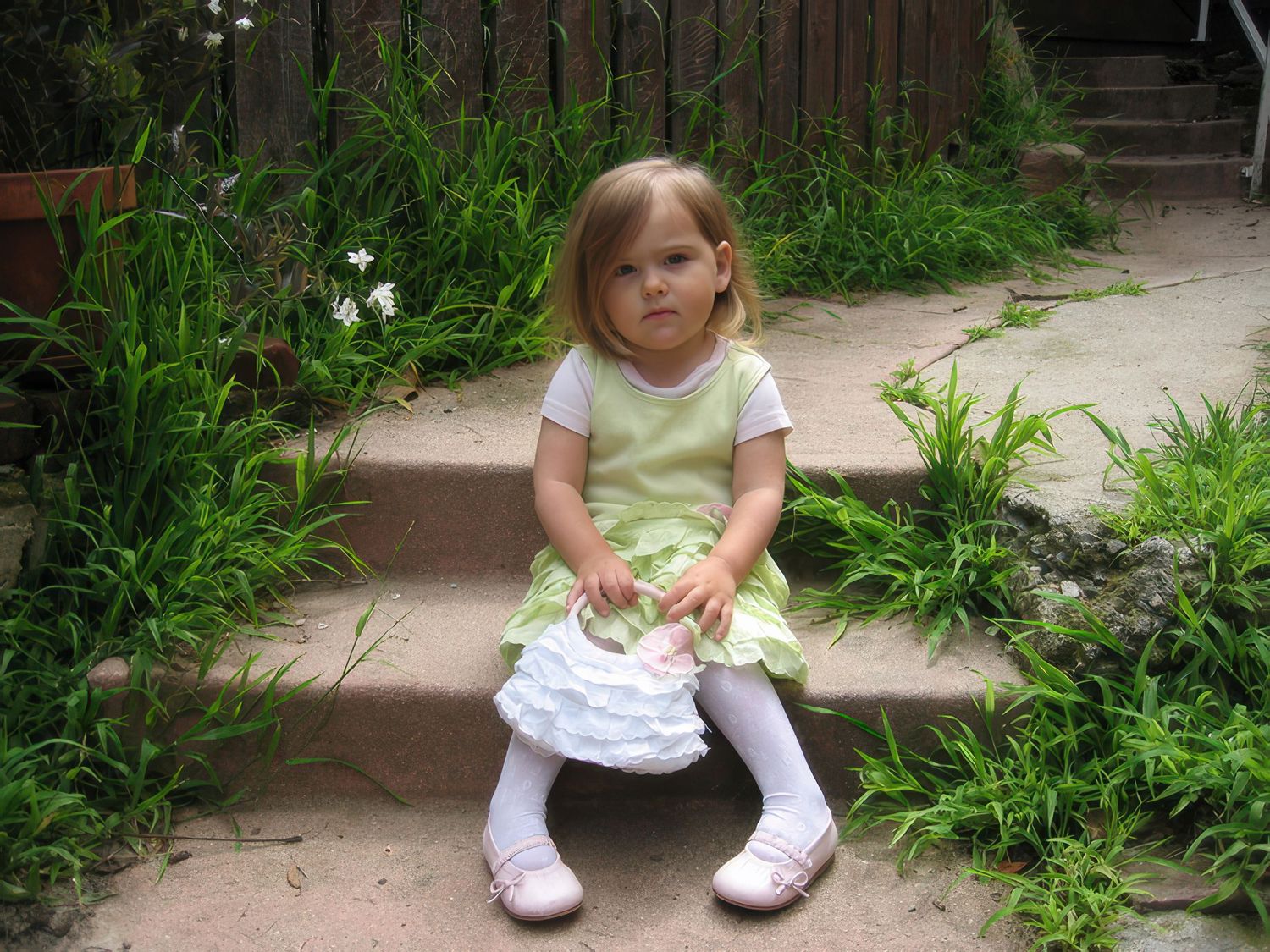 Child sitting on outdoor steps surrounded by green plants and foliage.