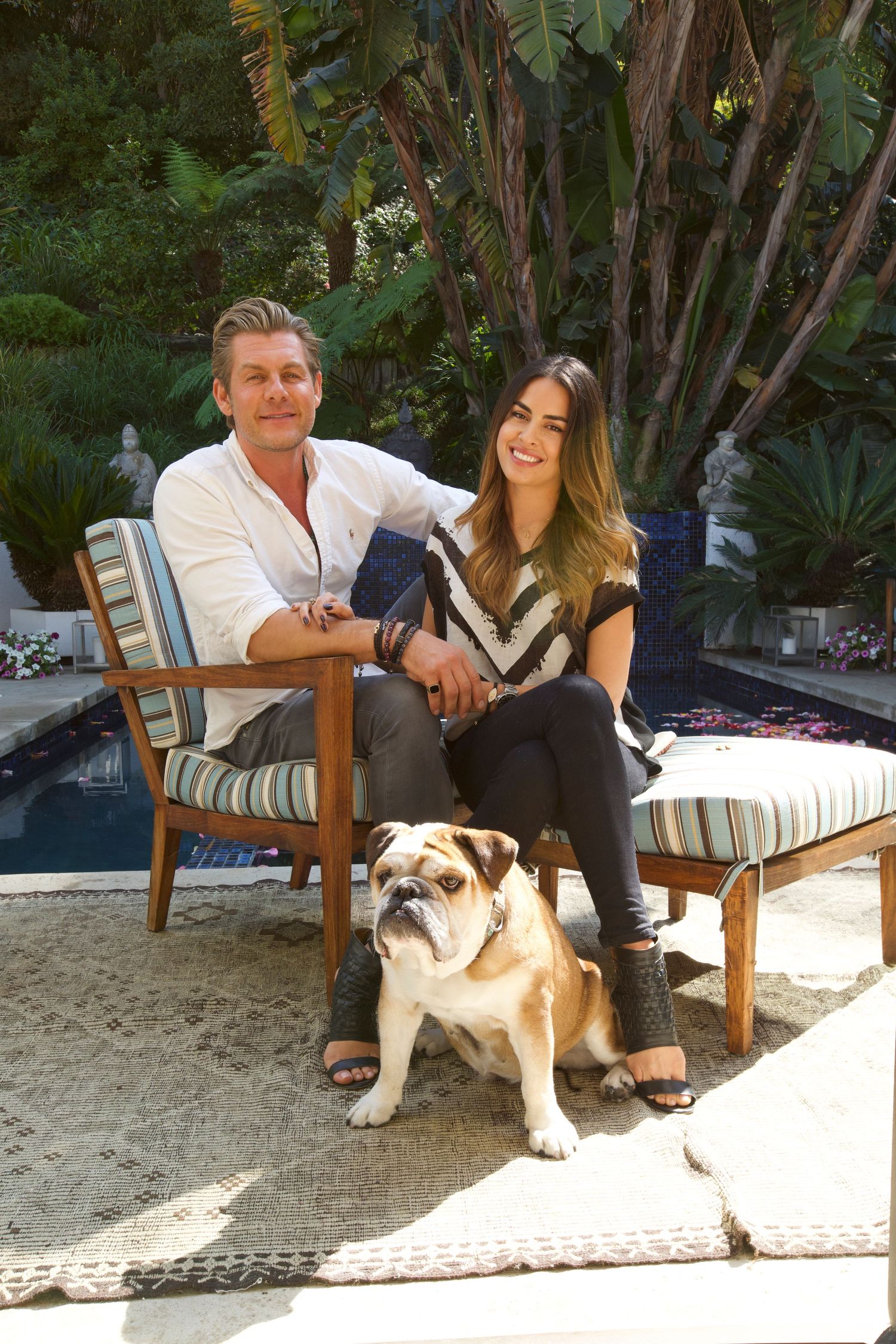 Casual outdoor portrait of couple relaxing with their bulldog on patio furniture.