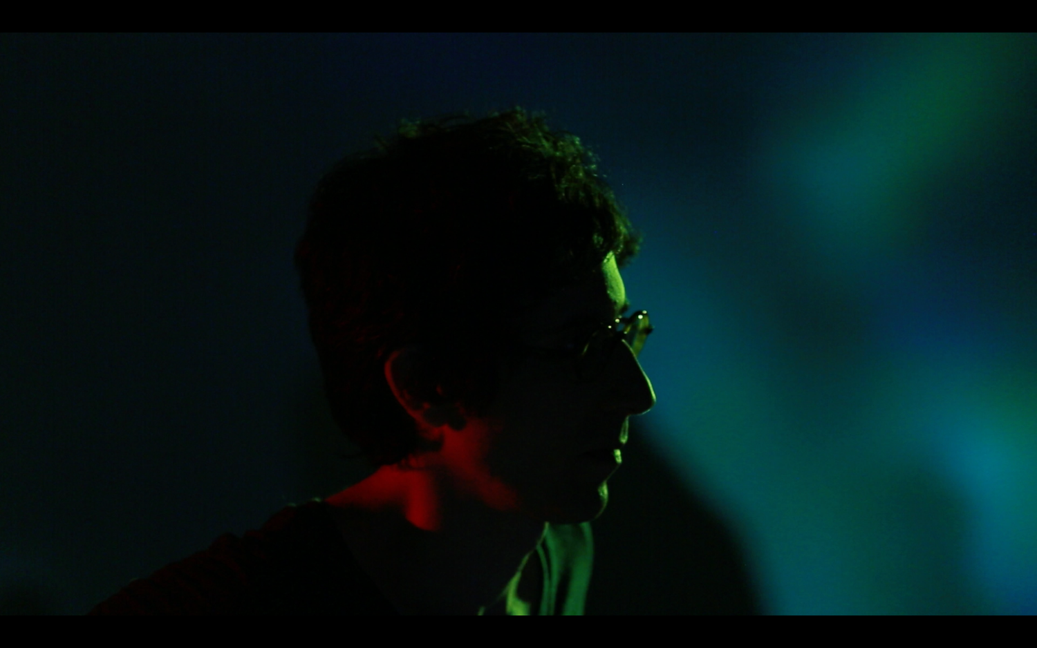 Atmospheric stage lighting creates moody silhouettes in shades of blue and green.