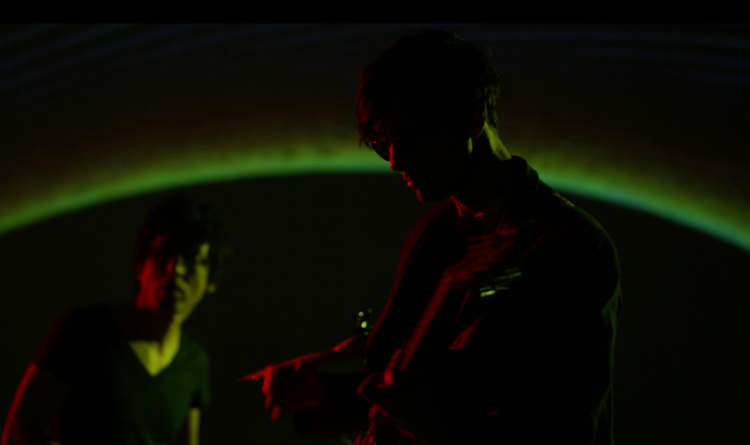 Concert performers in silhouette with dramatic red and green lighting effects.