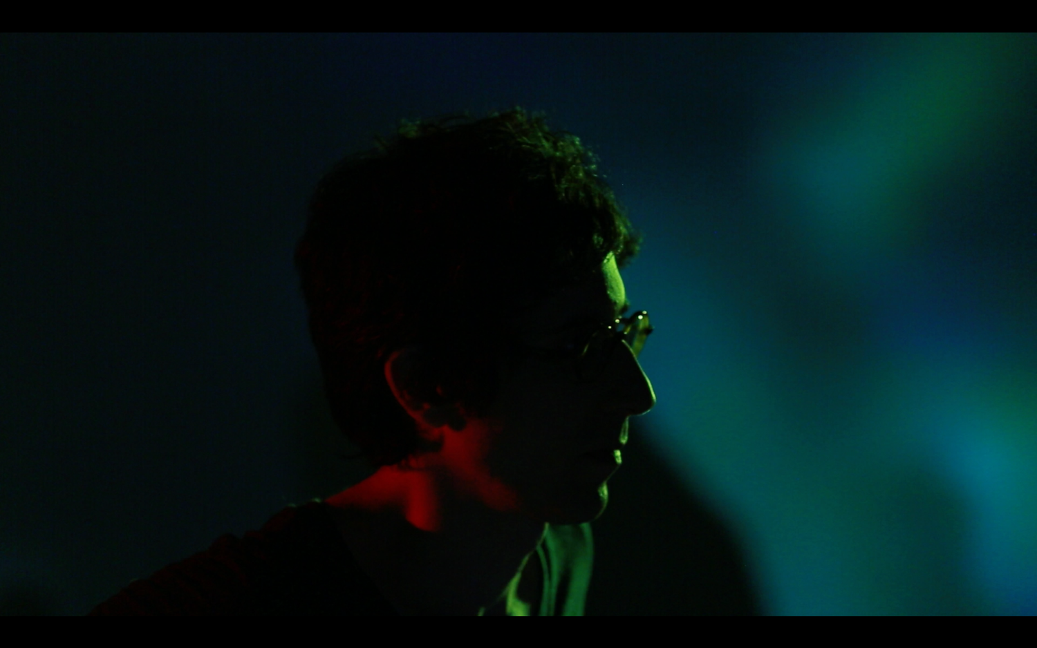 Dark silhouettes against a moody teal and black background with stage lighting.