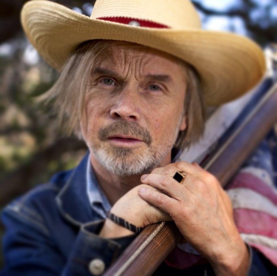 Portrait of person in cowboy hat holding musical instrument outdoors.