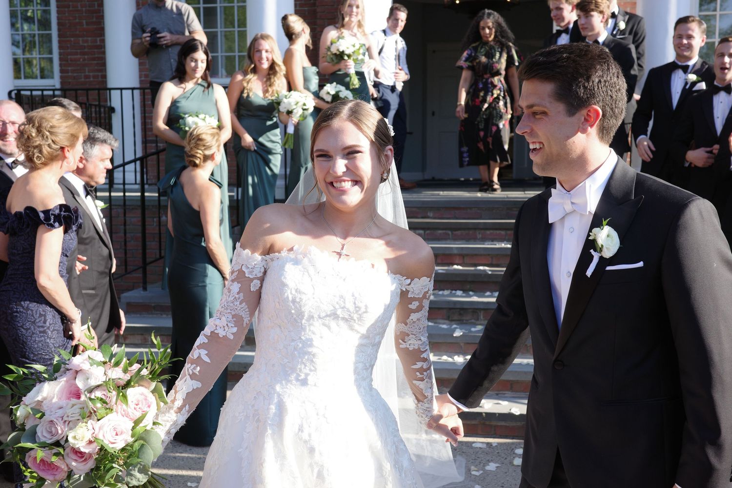 Wedding celebration outside a traditional building with guests in formal wear.