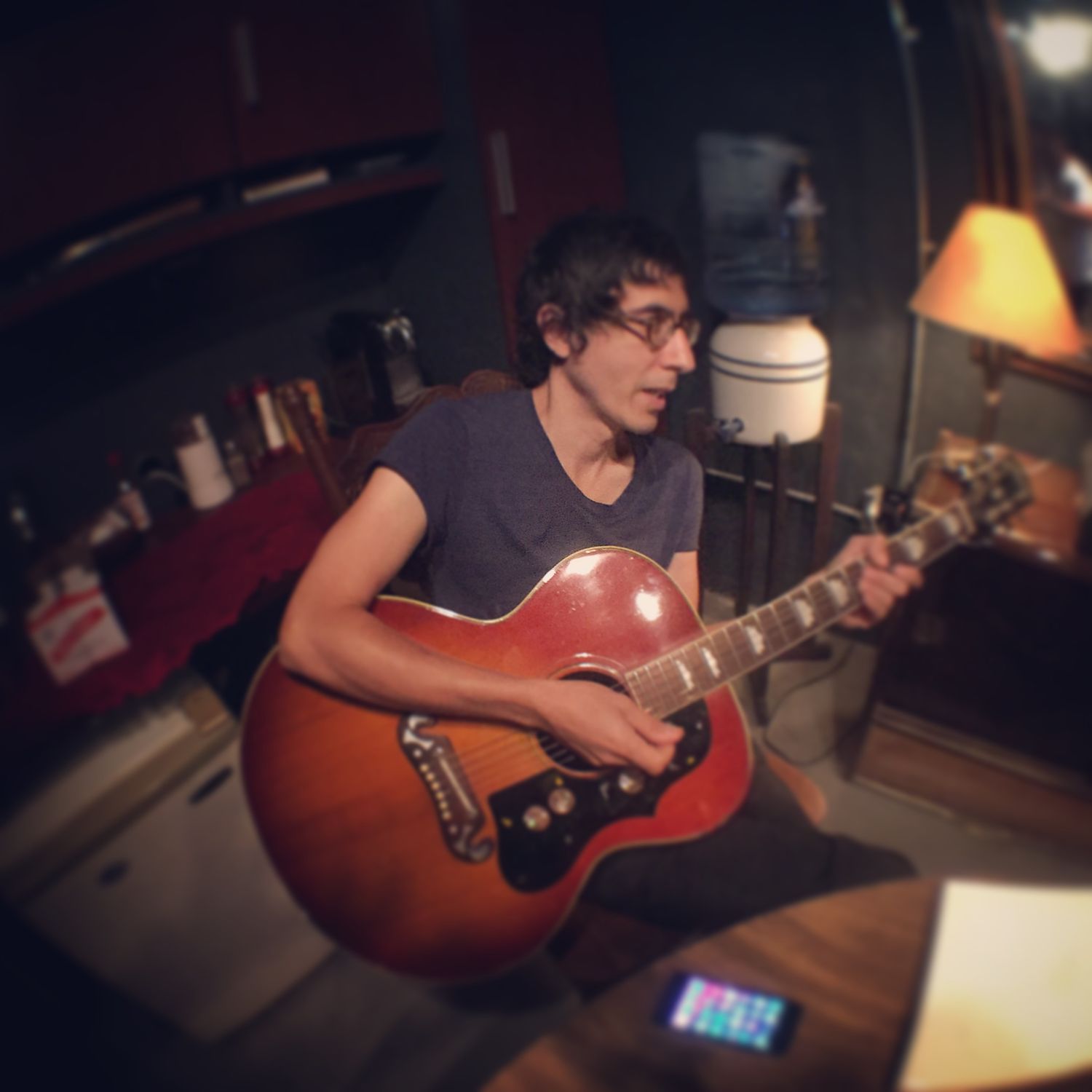 Musician playing acoustic guitar in dimly lit room with vintage film camera effect.