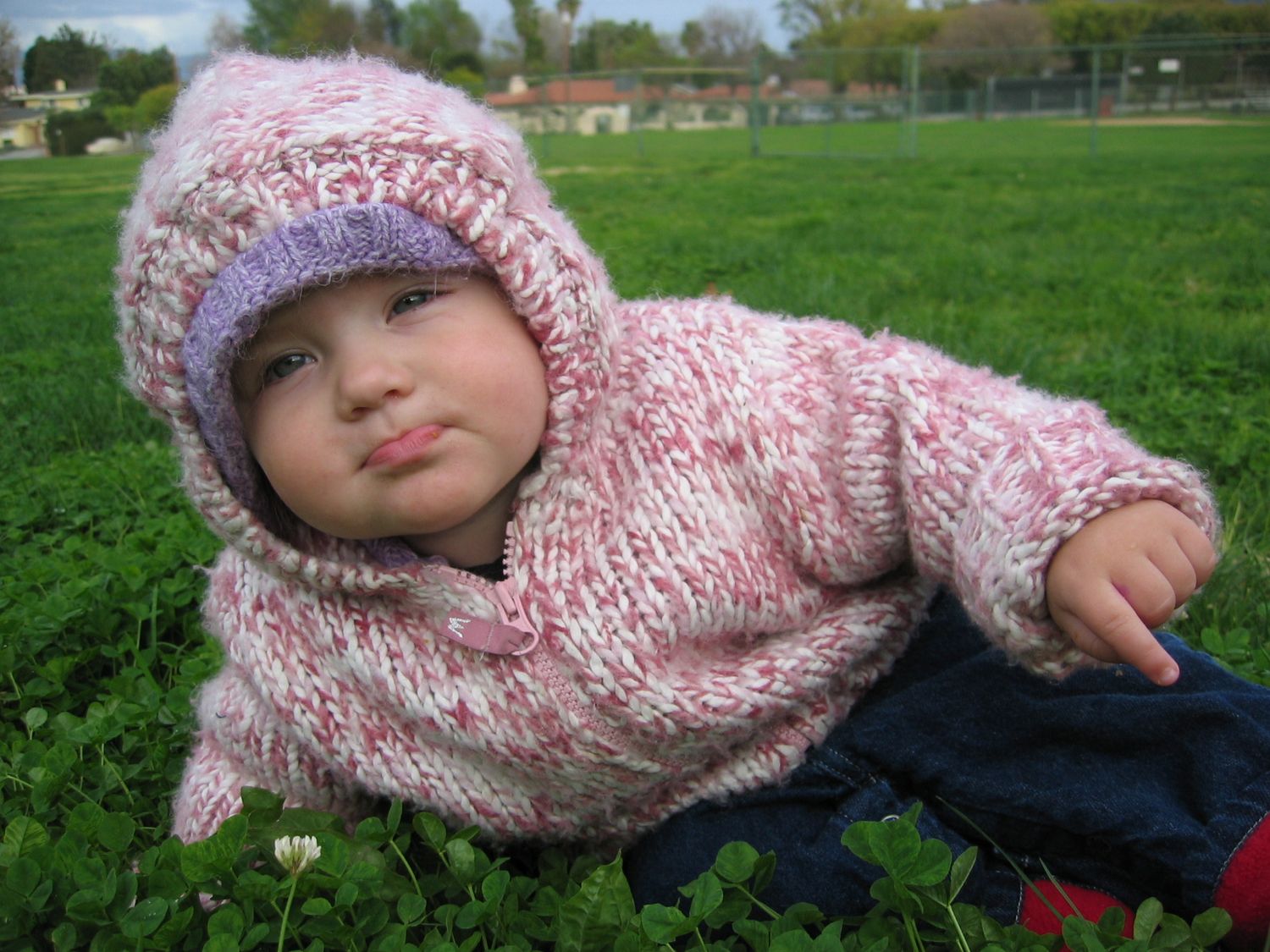 Child wearing pink knit sweater lying on grass outdoors.