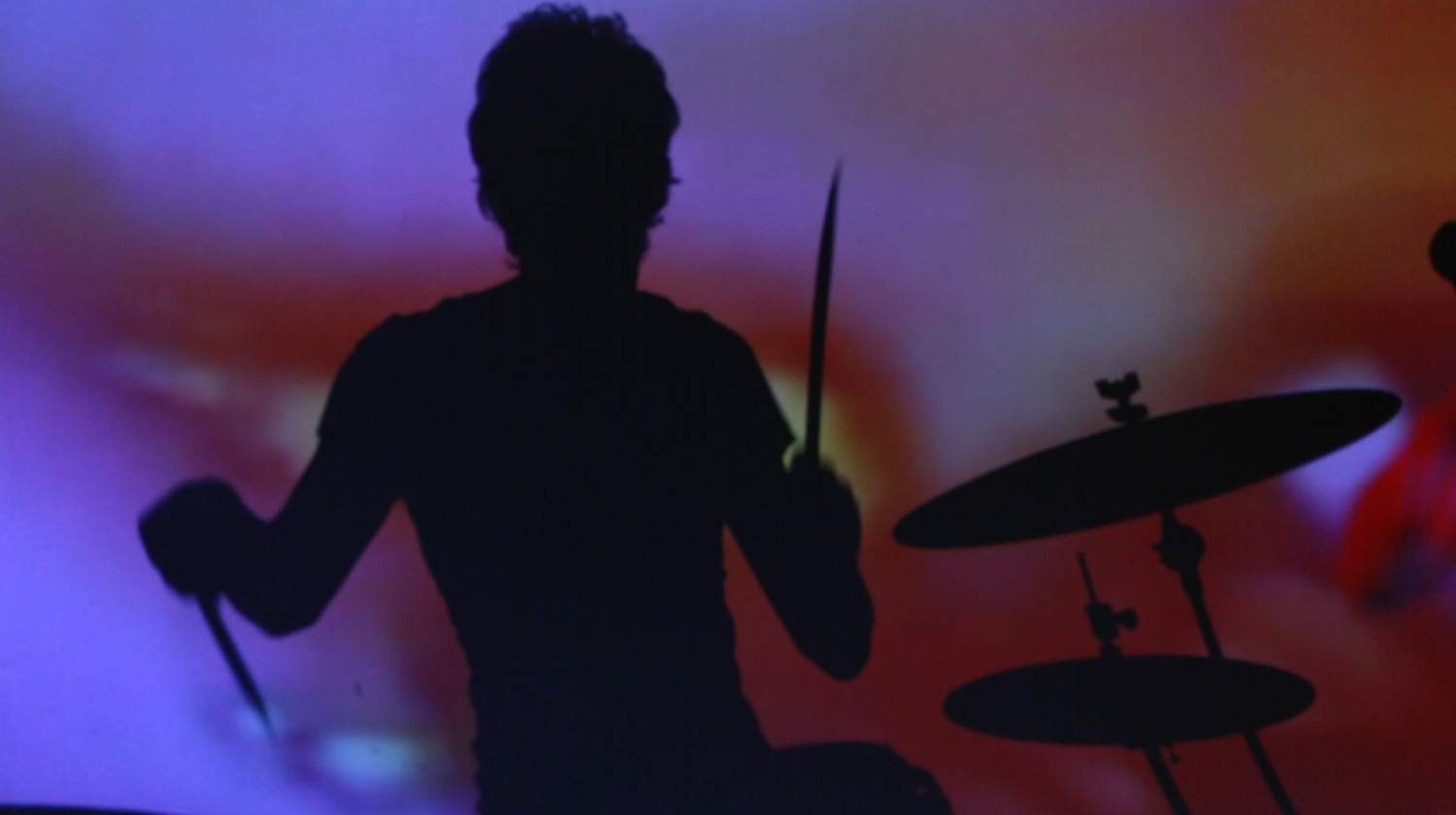 Band members in silhouette performing against blue and red stage lighting.