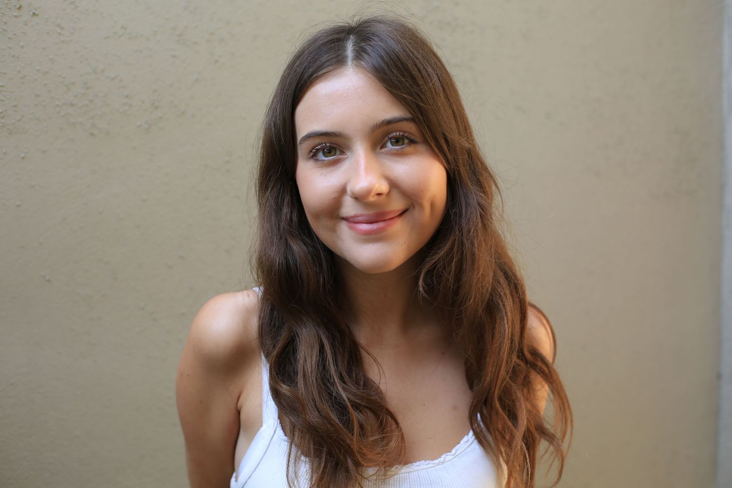 Woman in white top smiling against neutral background.