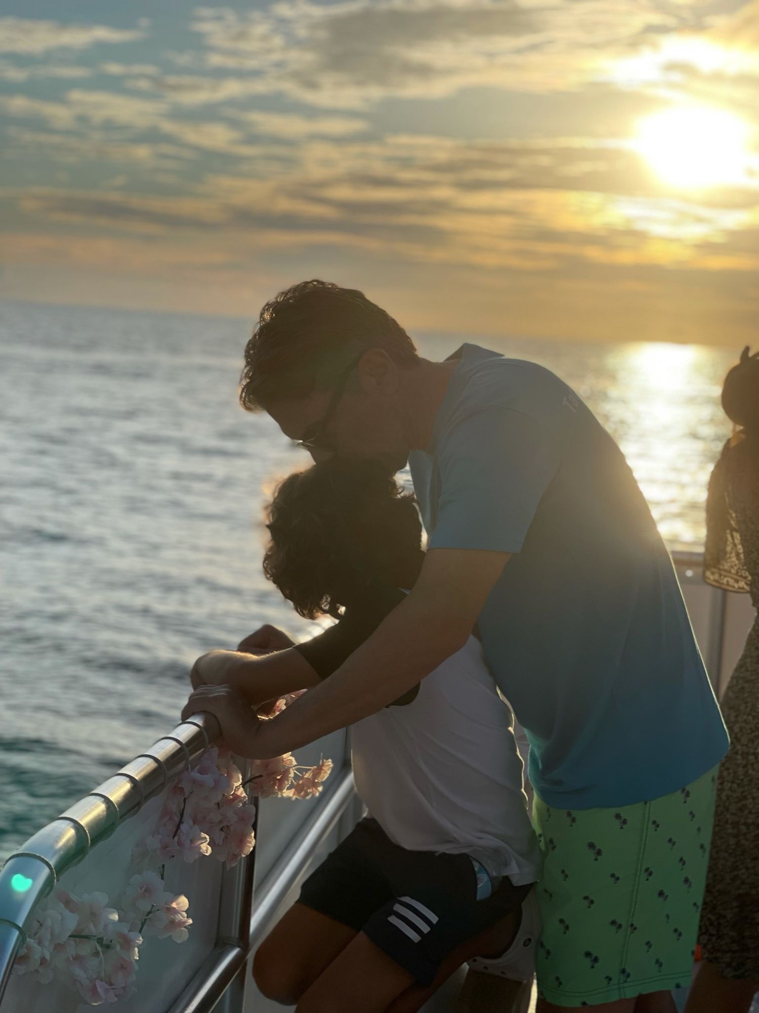 Person leaning on boat railing at sunset over ocean with golden light reflecting on water.