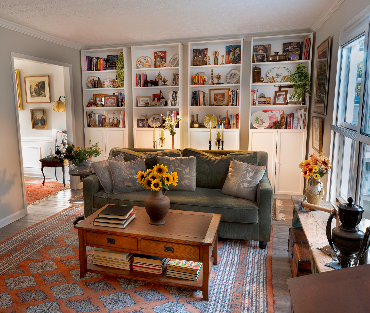 Cozy living room with gray sofa, sunflowers, wooden coffee table, and white built-in bookshelves on a colorful rug.
