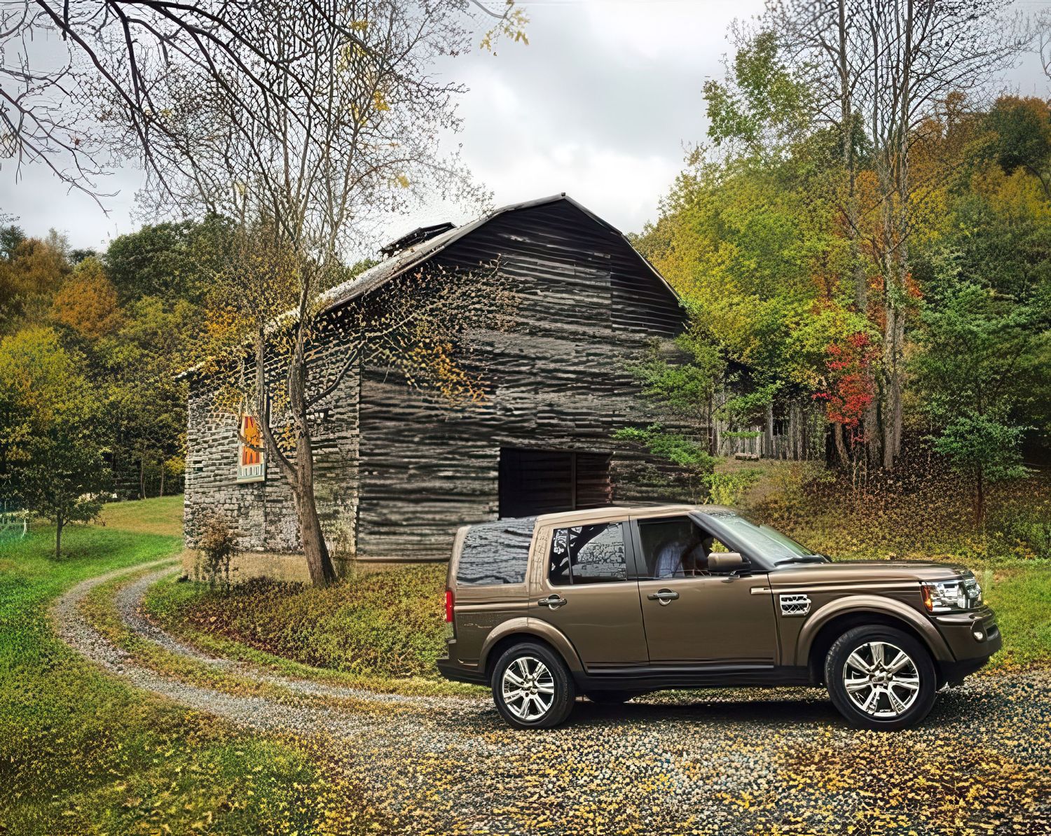 Autumn landscape with old log cabin and SUV on winding dirt road surrounded by fall foliage.