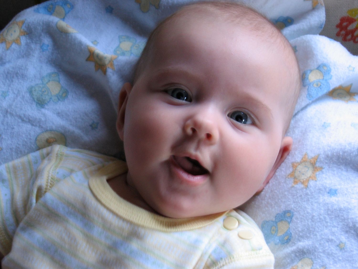 Smiling infant lying on blue patterned blanket wearing yellow onesie.