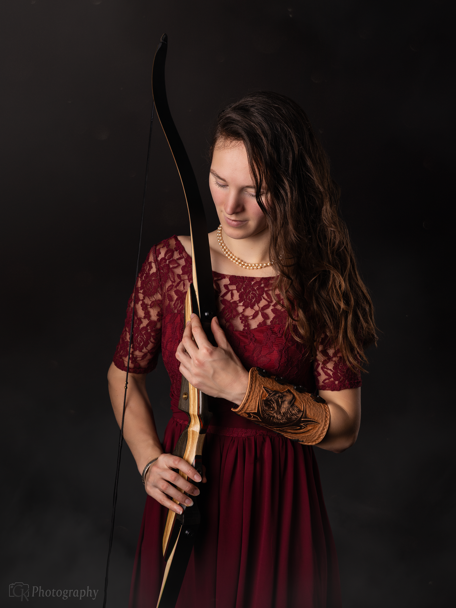 Artistiek studio portret van vrouw in elegante bordeaux jurk met kant en een boog, met een tijdloze en krachtige uitstraling