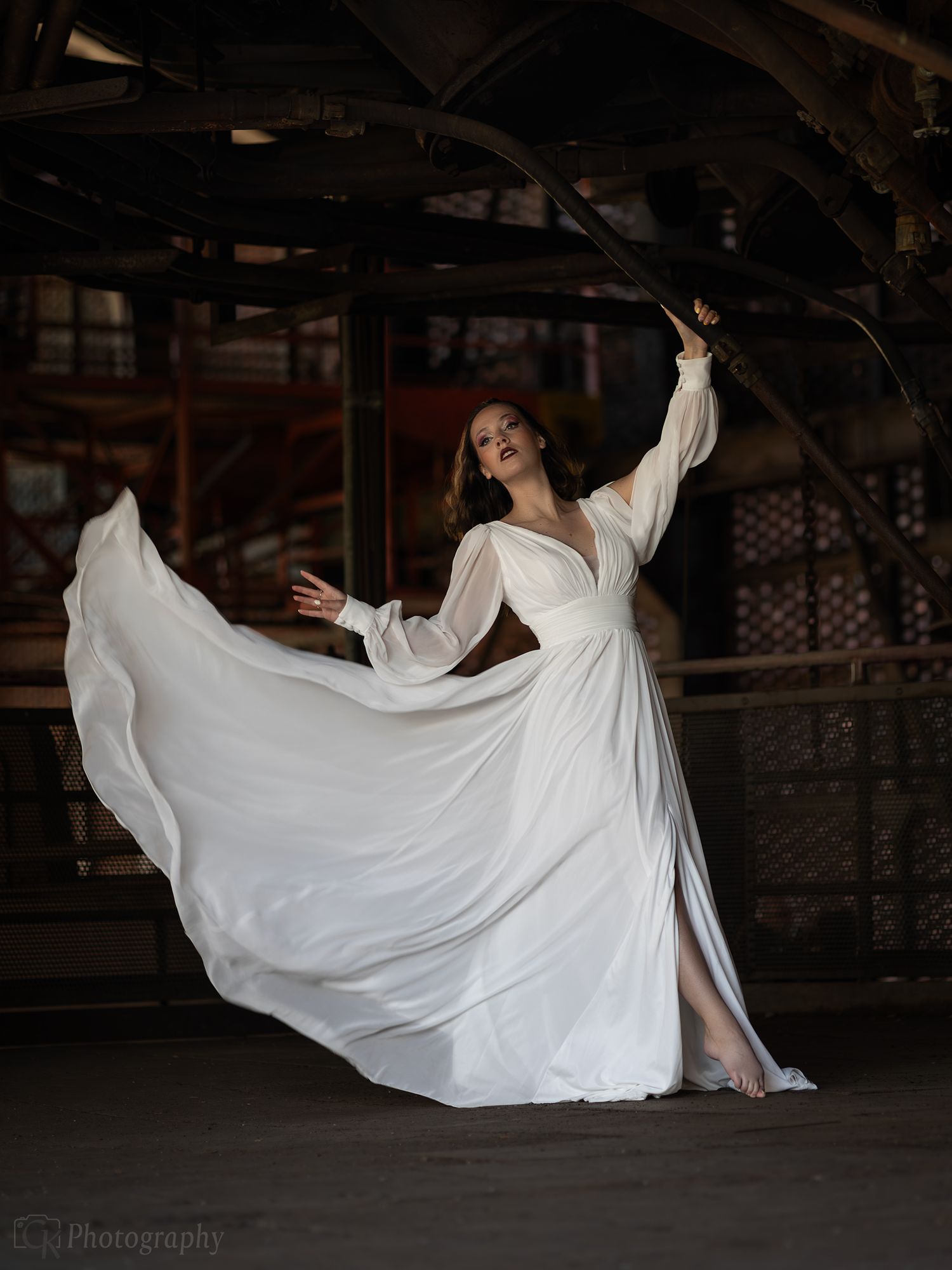 Elegante portretfotografie van een model in een witte designerjurk tegen een industriële achtergrond