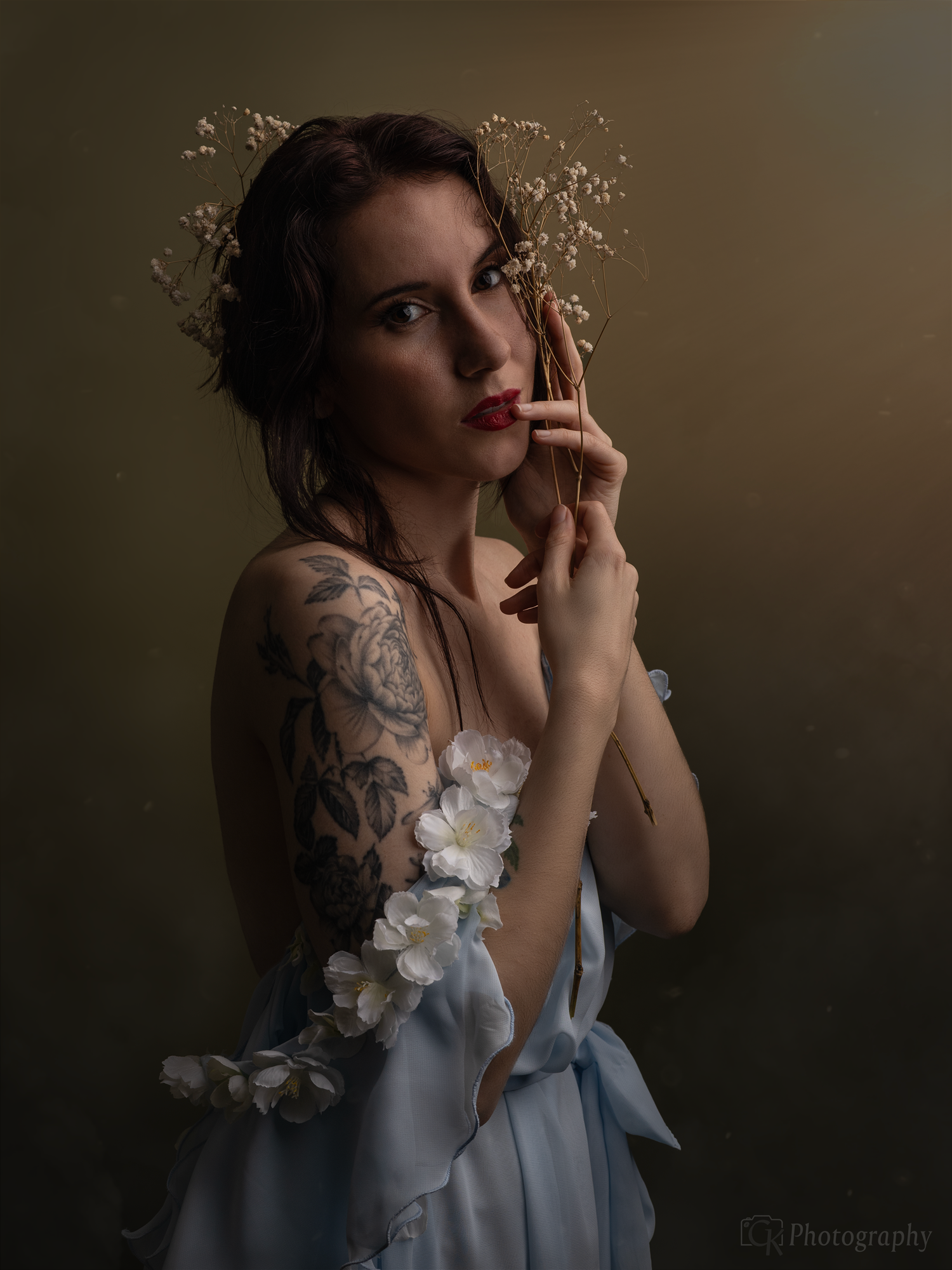 Sfeervol studio portret van vrouw in lichtblauwe jurk met bloemen accessoire en zachte beige achtergrond