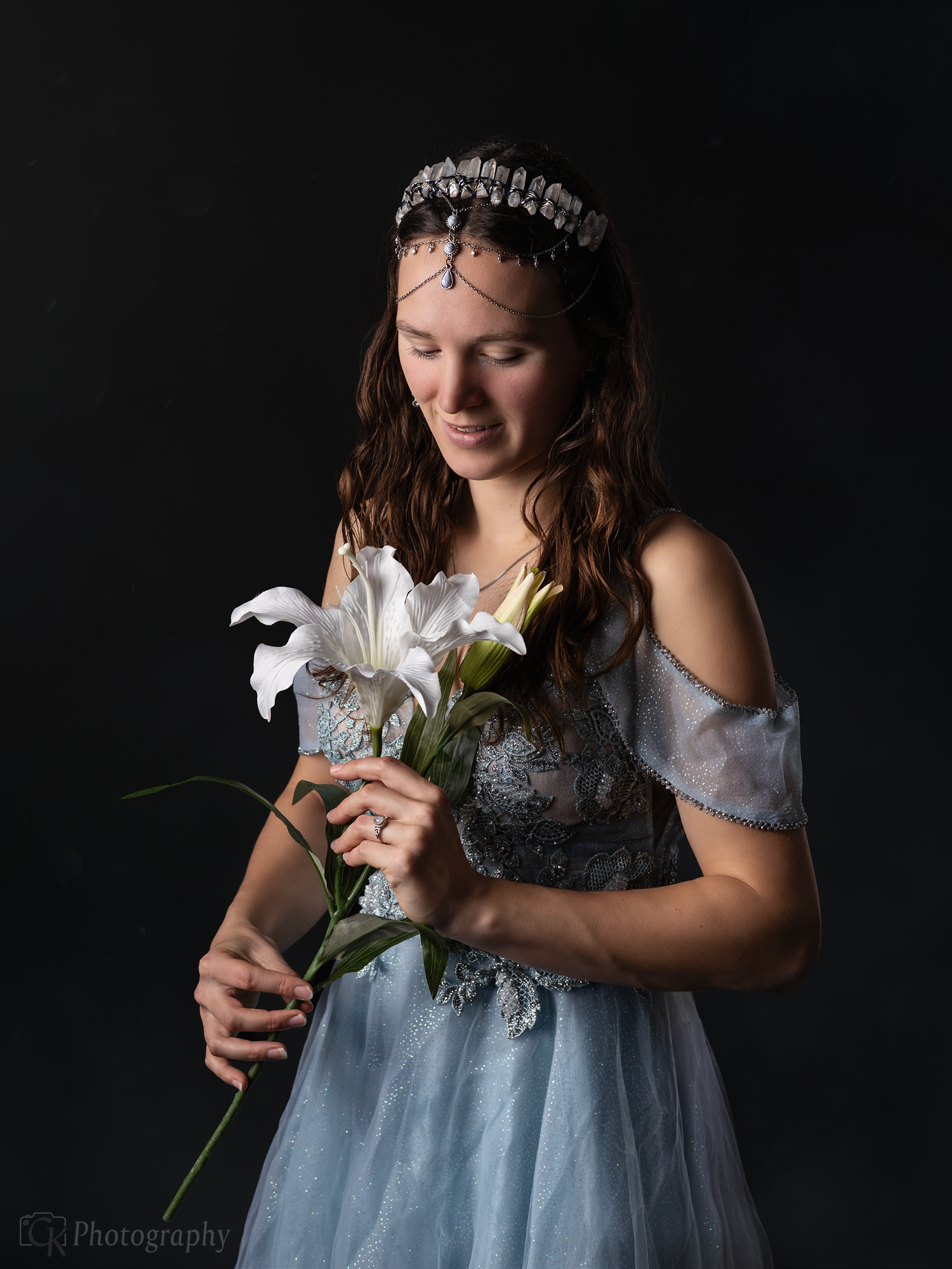 Fantasy geïnspireerd studio portret van vrouw in blauwe prinsessenjurk met kristallen haarstuk en witte lelie