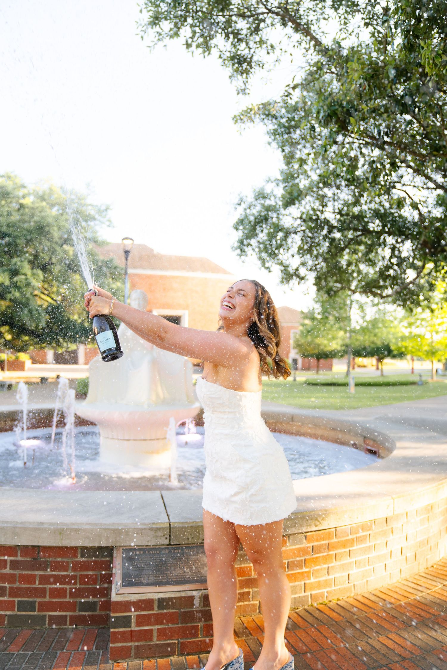 Person in white outfit playing in outdoor fountain water spray.
