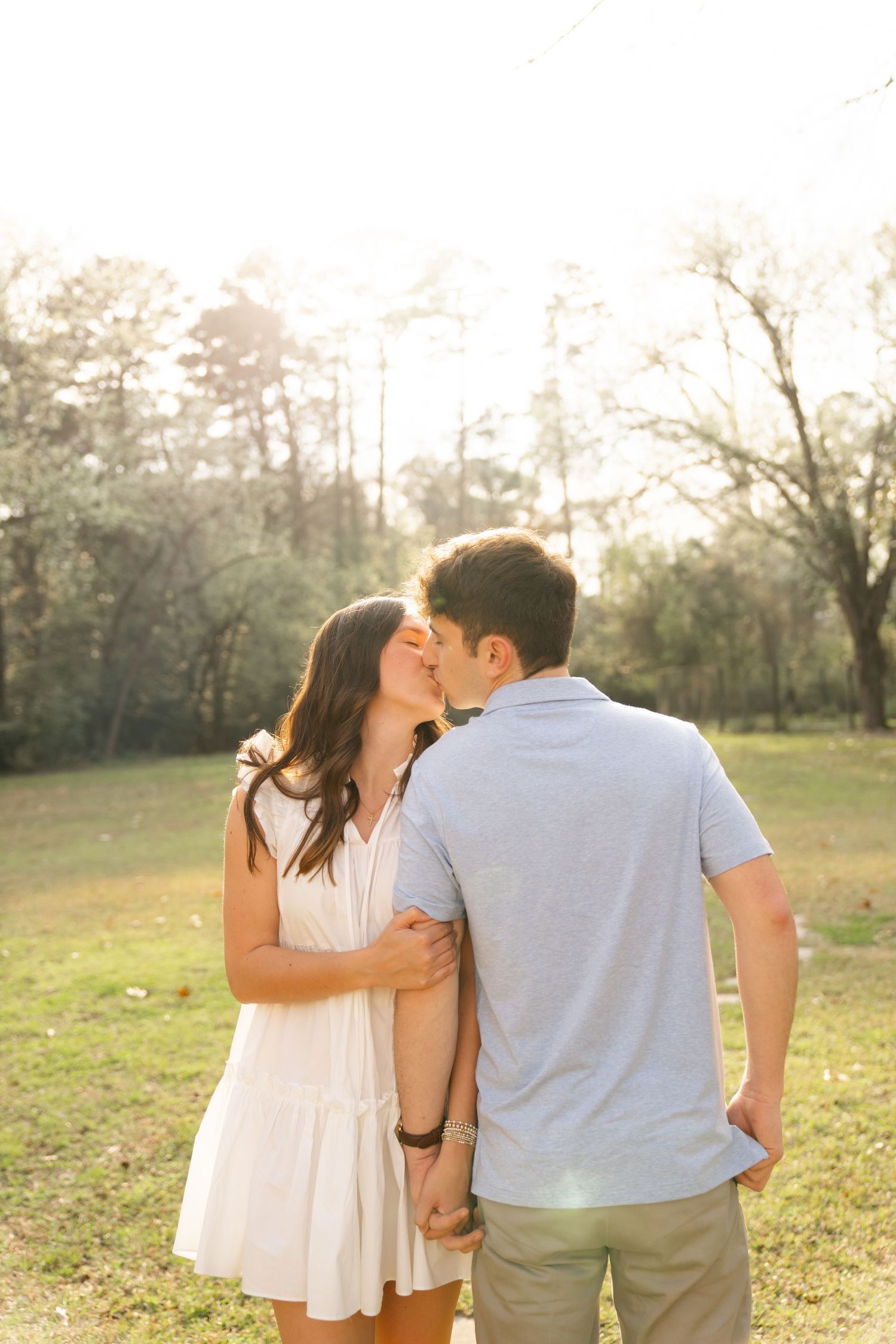 Couple in light summer outfits embracing in golden sunlit field.