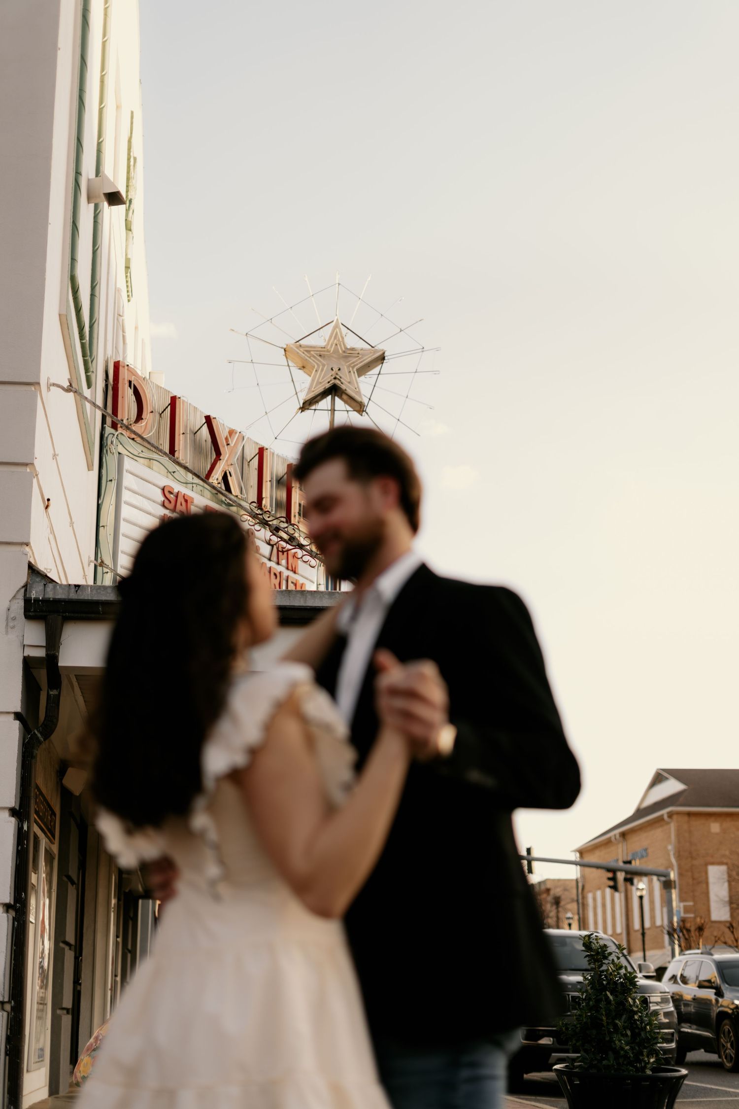 Silhouetted couple dancing in an urban setting at dusk with vintage storefronts in background.