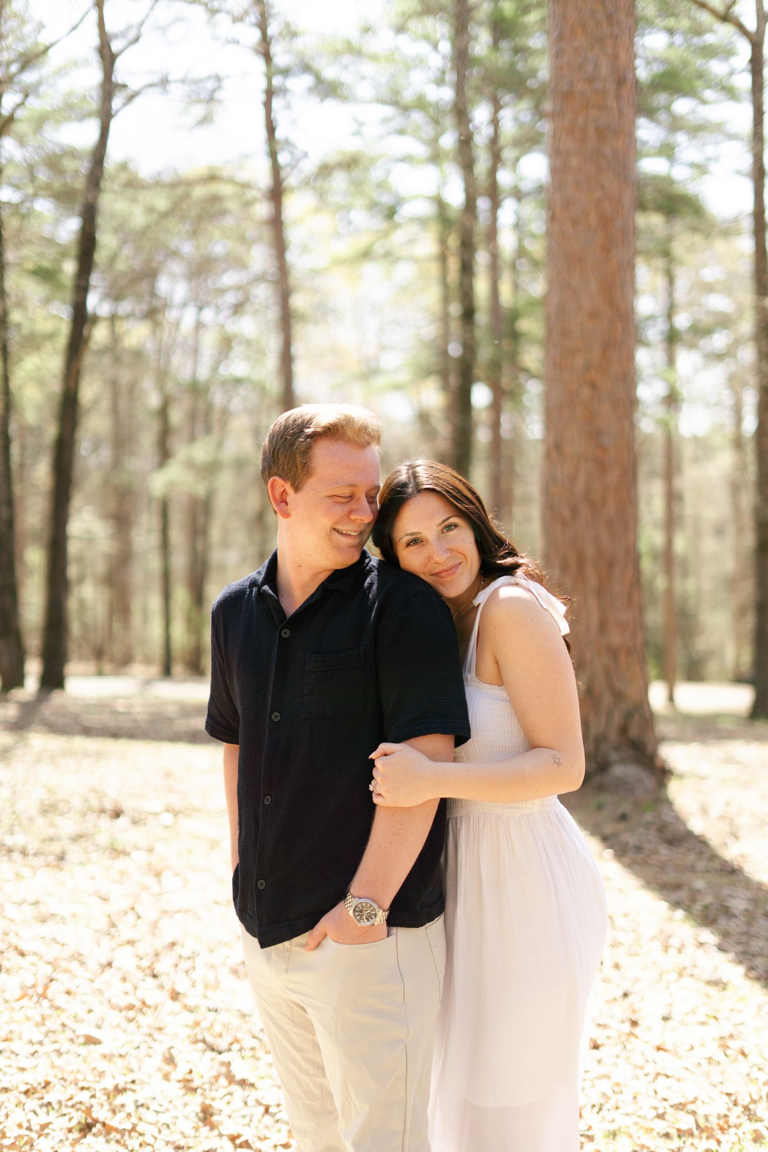 A couple shares romantic moments in a sun-dappled pine forest during their wedding photography session.